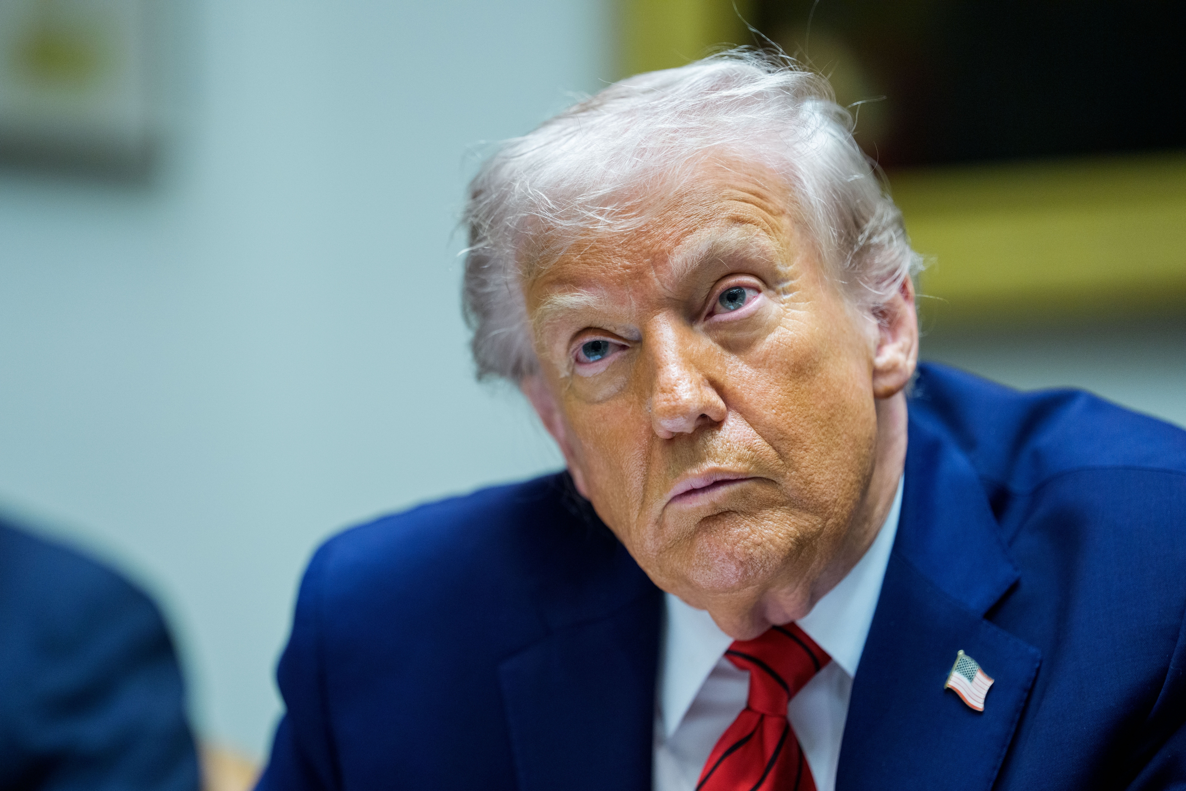 En person i dress med en amerikansk flaggnål sitter på et møte og ser innadvendt ut