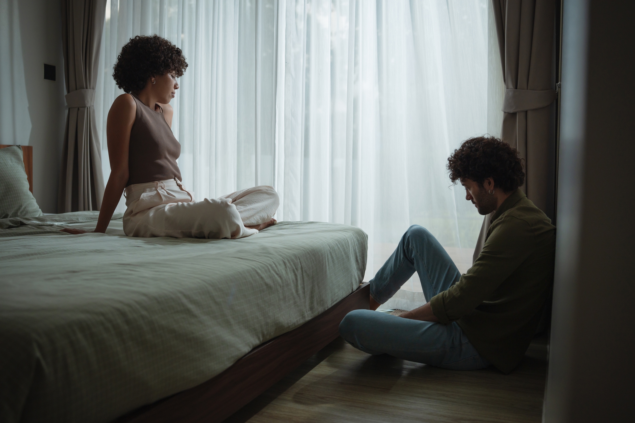 Two radical   are successful  a dimly-lit bedroom; 1  sits connected  the bed, the different   connected  the floor, some  appearing heavy  successful  thought