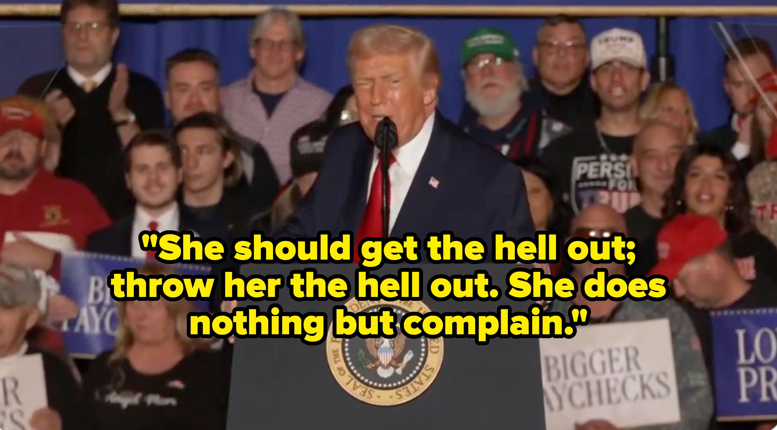 Person som snakker på et podium foran en folkemengde som holder skilt