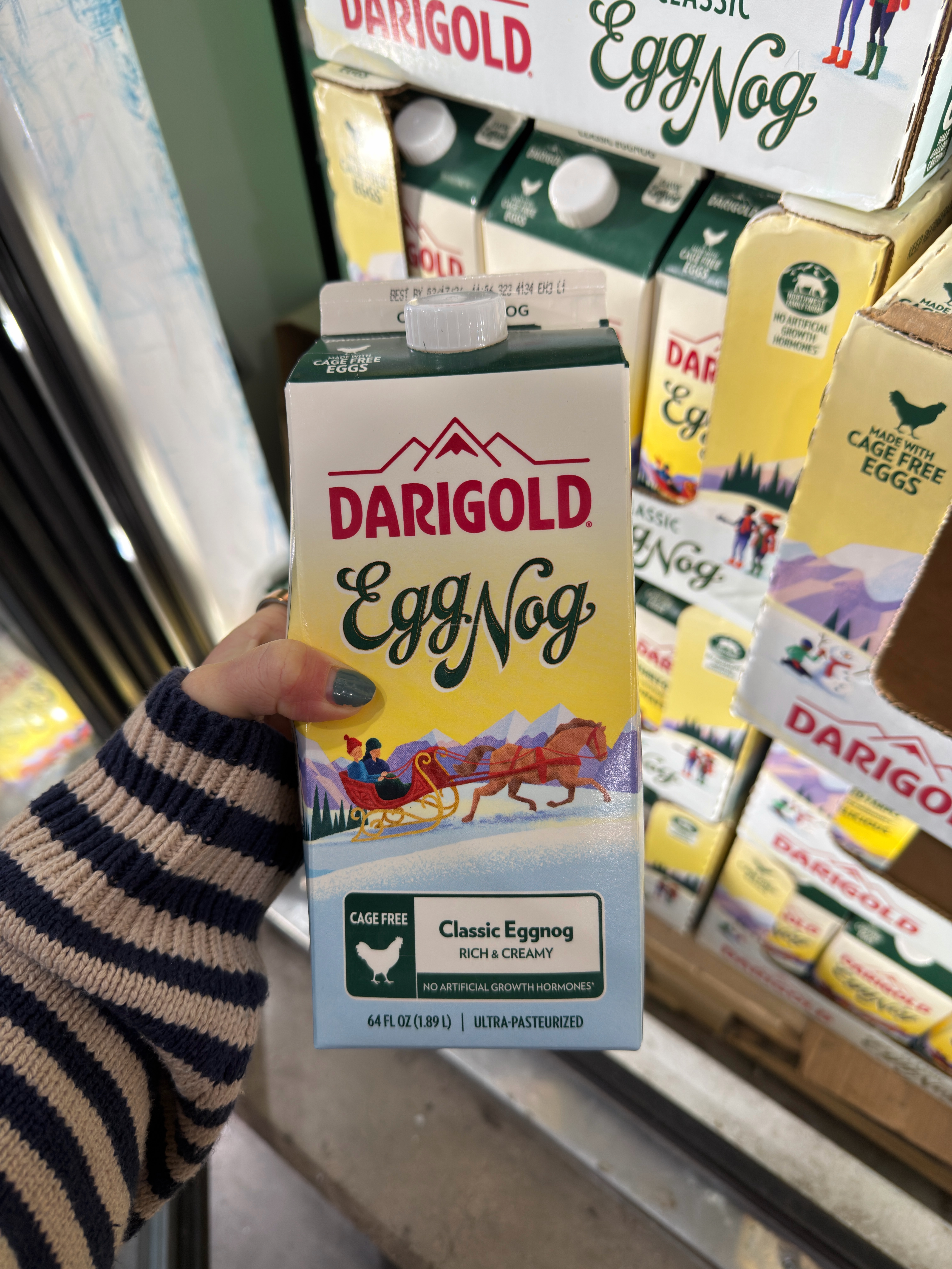 Person holding a carton of Darigold Classic Eggnog in a store, with other cartons visible on the shelf