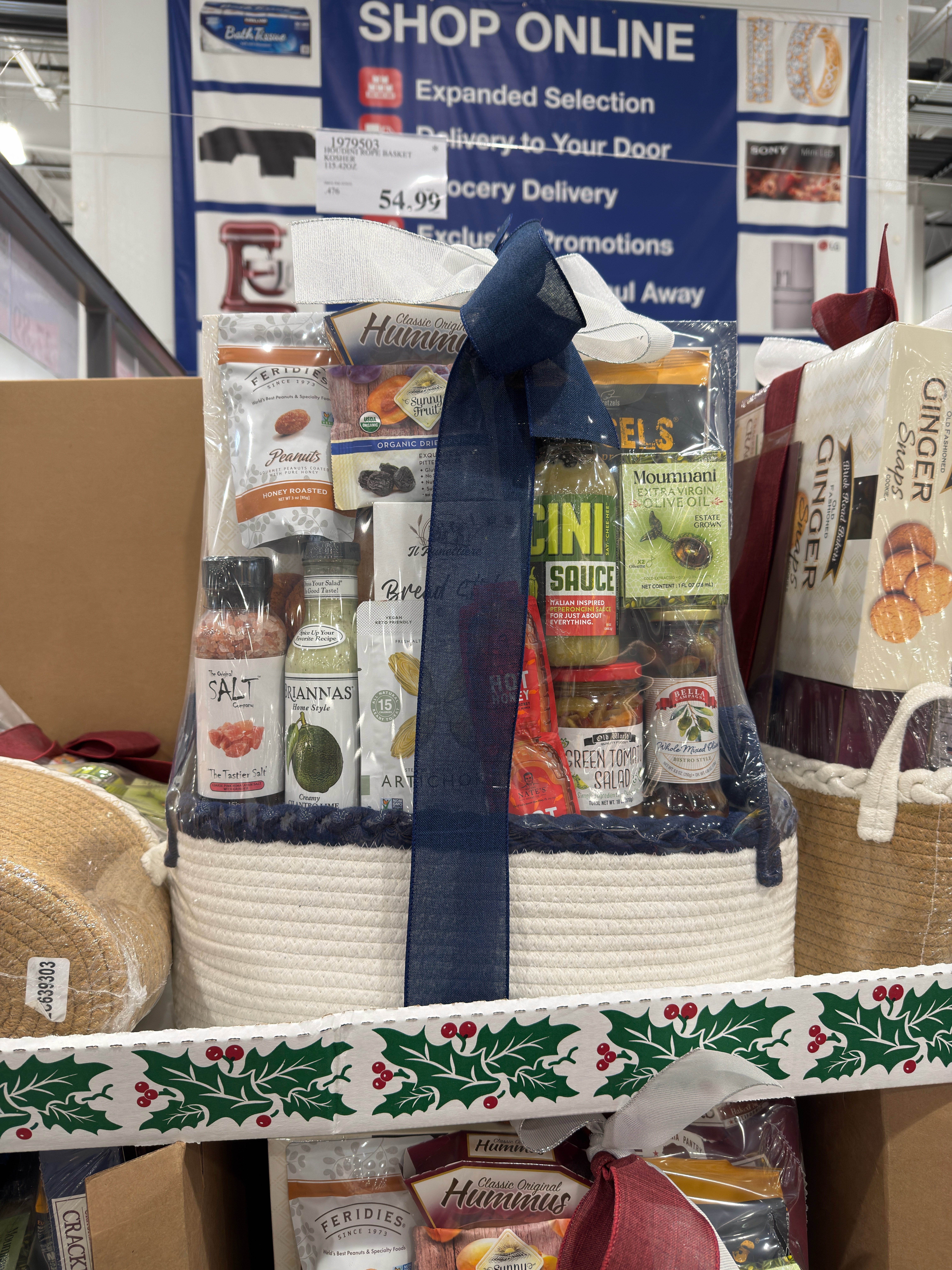 Gourmet gift basket with assorted snacks, sauces, and treats displayed in a store, wrapped with a dark bow