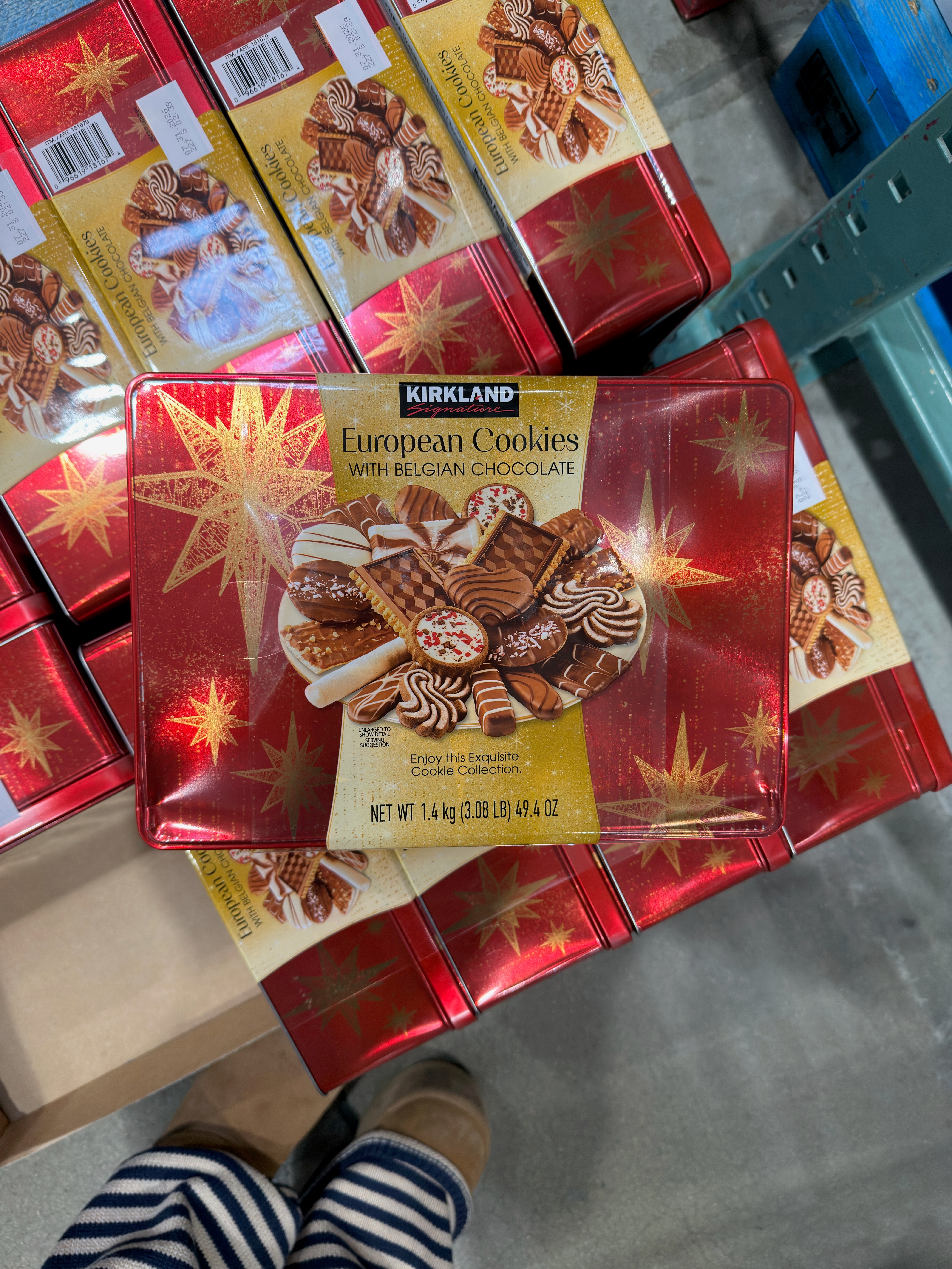 A person holds a Kirkland European Cookies tin with Belgian chocolate, featuring assorted cookies on the packaging, in a store setting