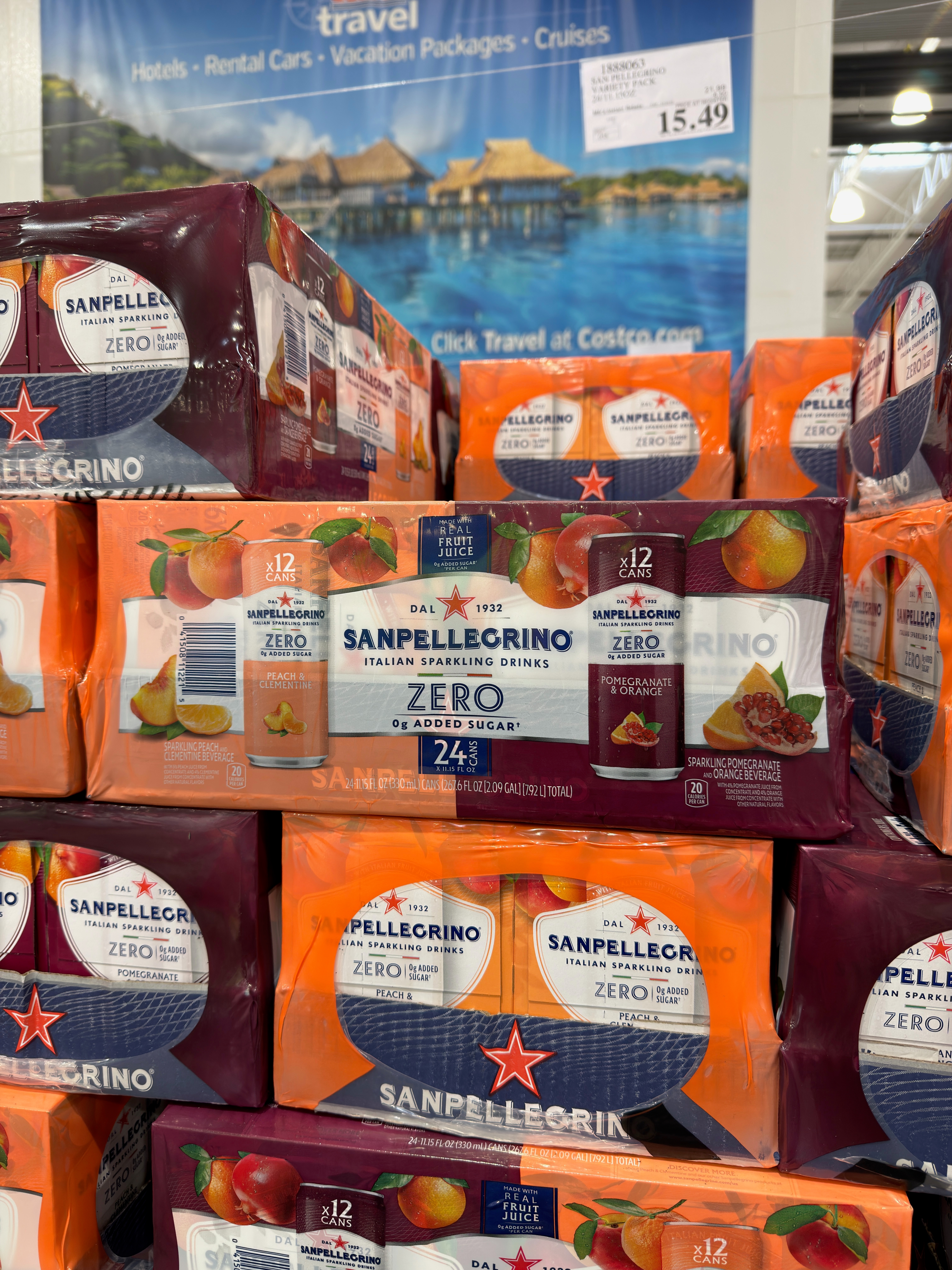 Sanpellegrino Zero sparkling drinks in 24-pack boxes are stacked in store. Travel brochures and cruise offers visible in the background
