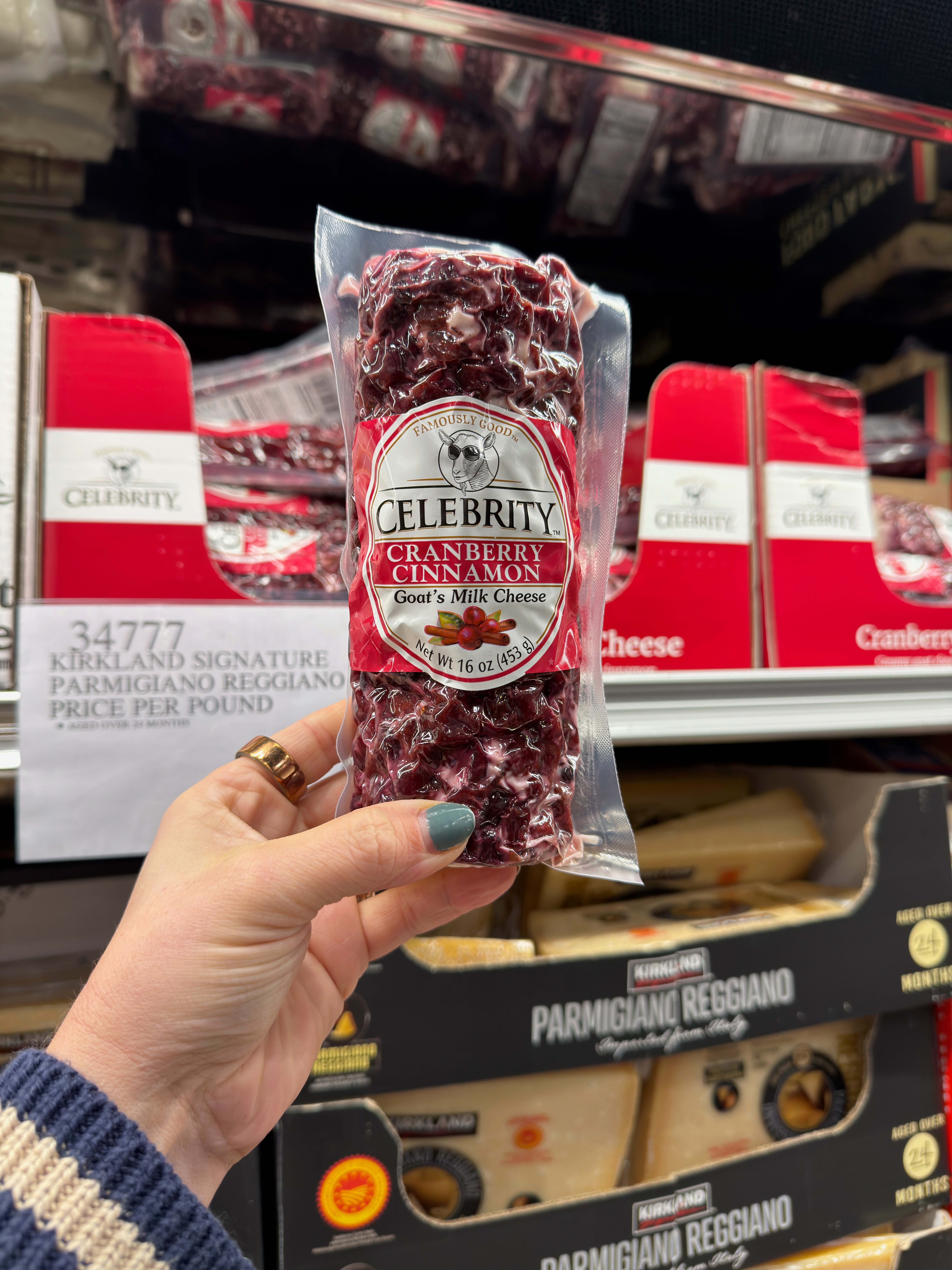 Hand holding a package of Celebrity cranberry cinnamon goat's milk cheese in a store aisle with cheese displays in the background