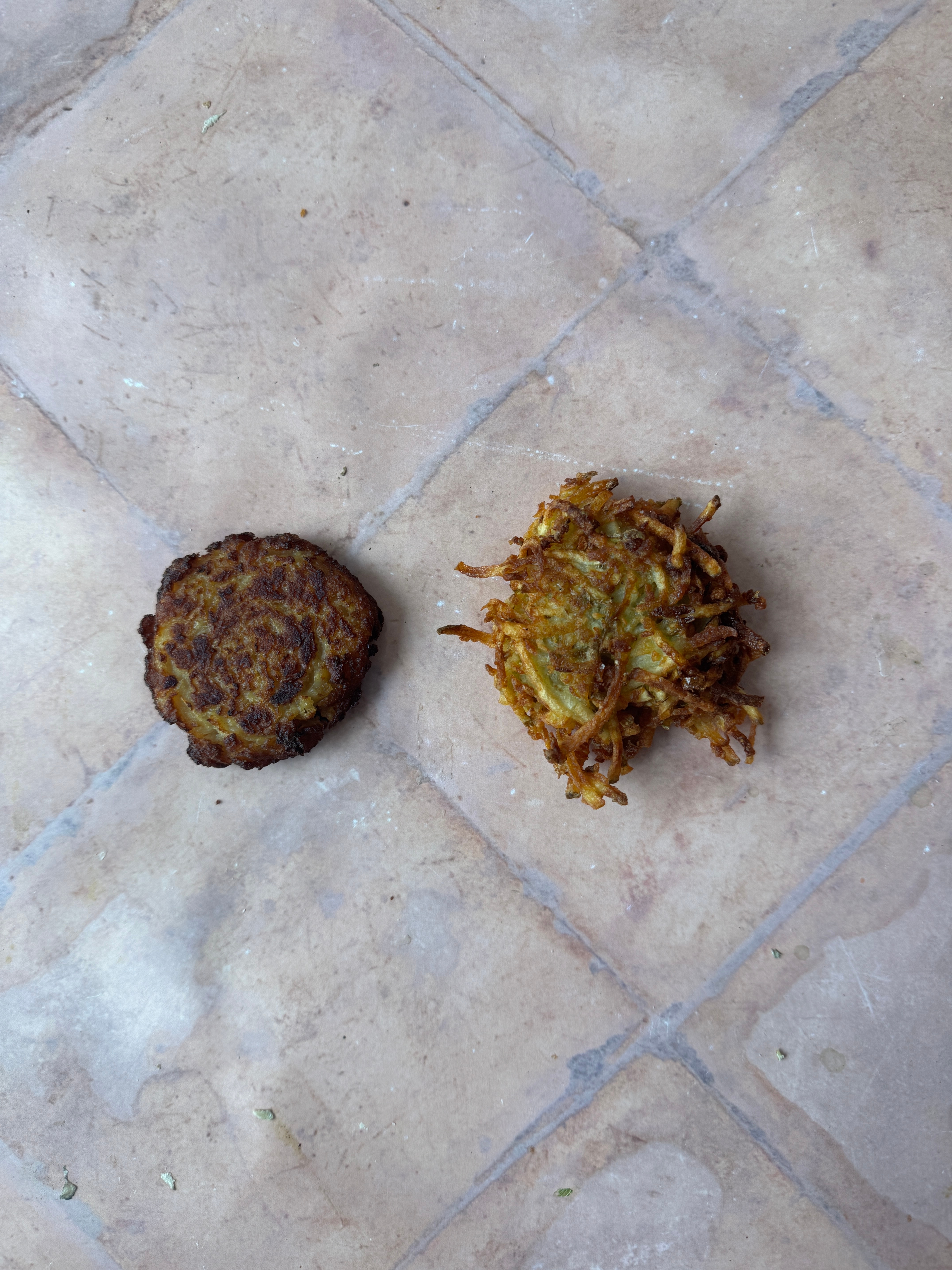 Two fritters on a tile surface, a smooth, compact one on the left and a loose, crispy one on the right