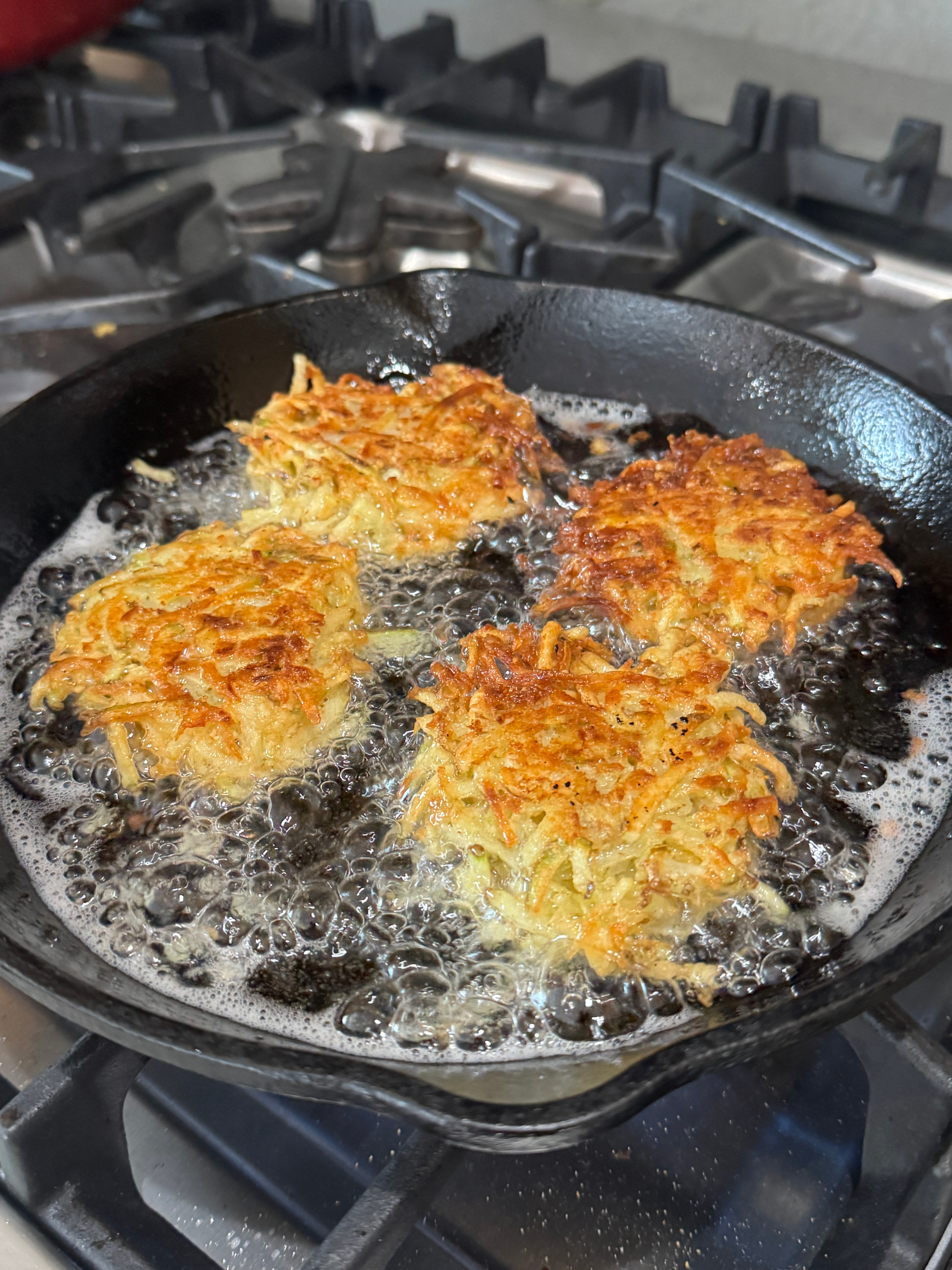 Four crispy potato pancakes frying in a cast iron skillet on a stove