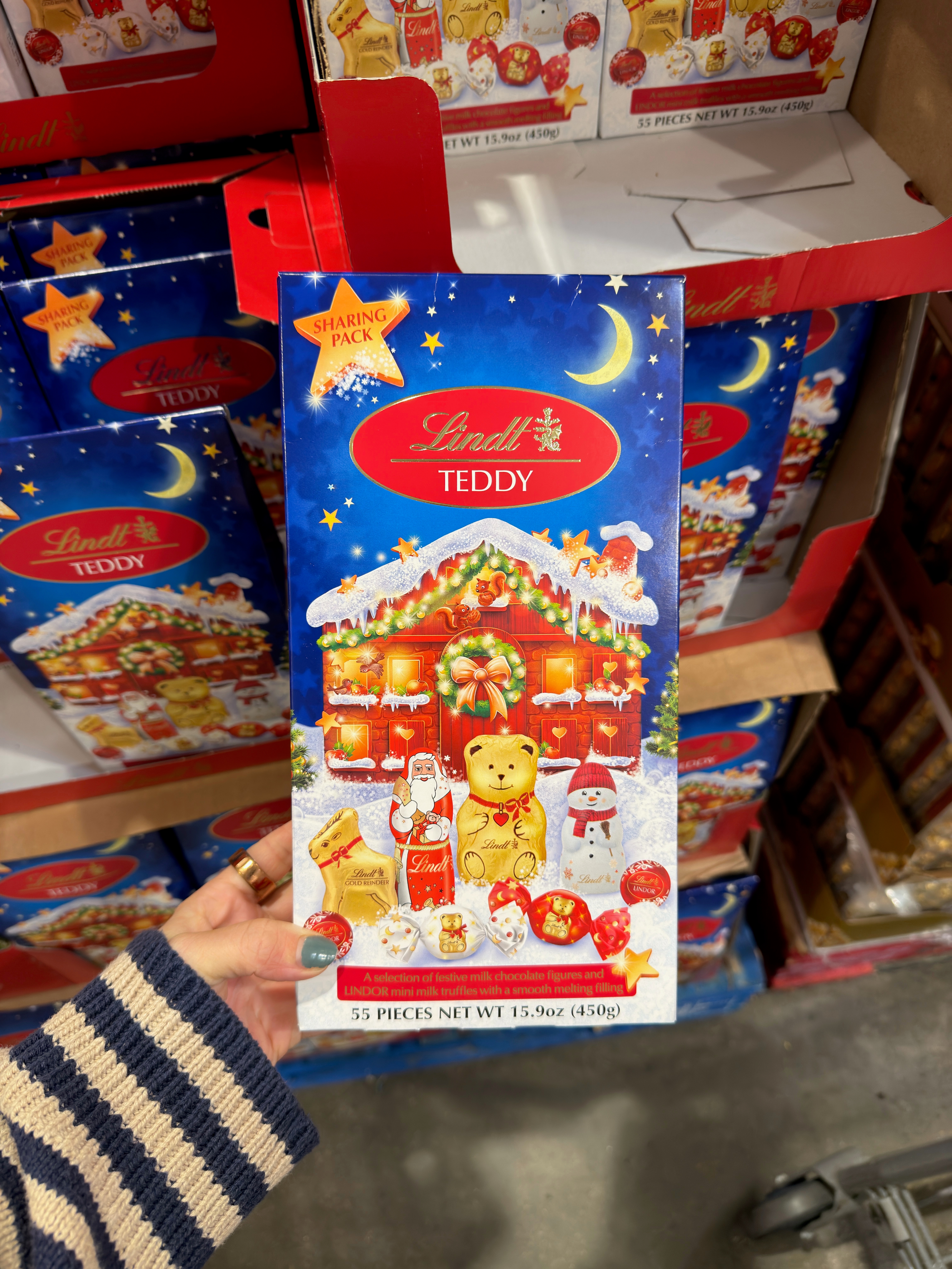 Person holding a Lindt Teddy chocolate box featuring a festive winter scene with teddy bears and Santa Claus