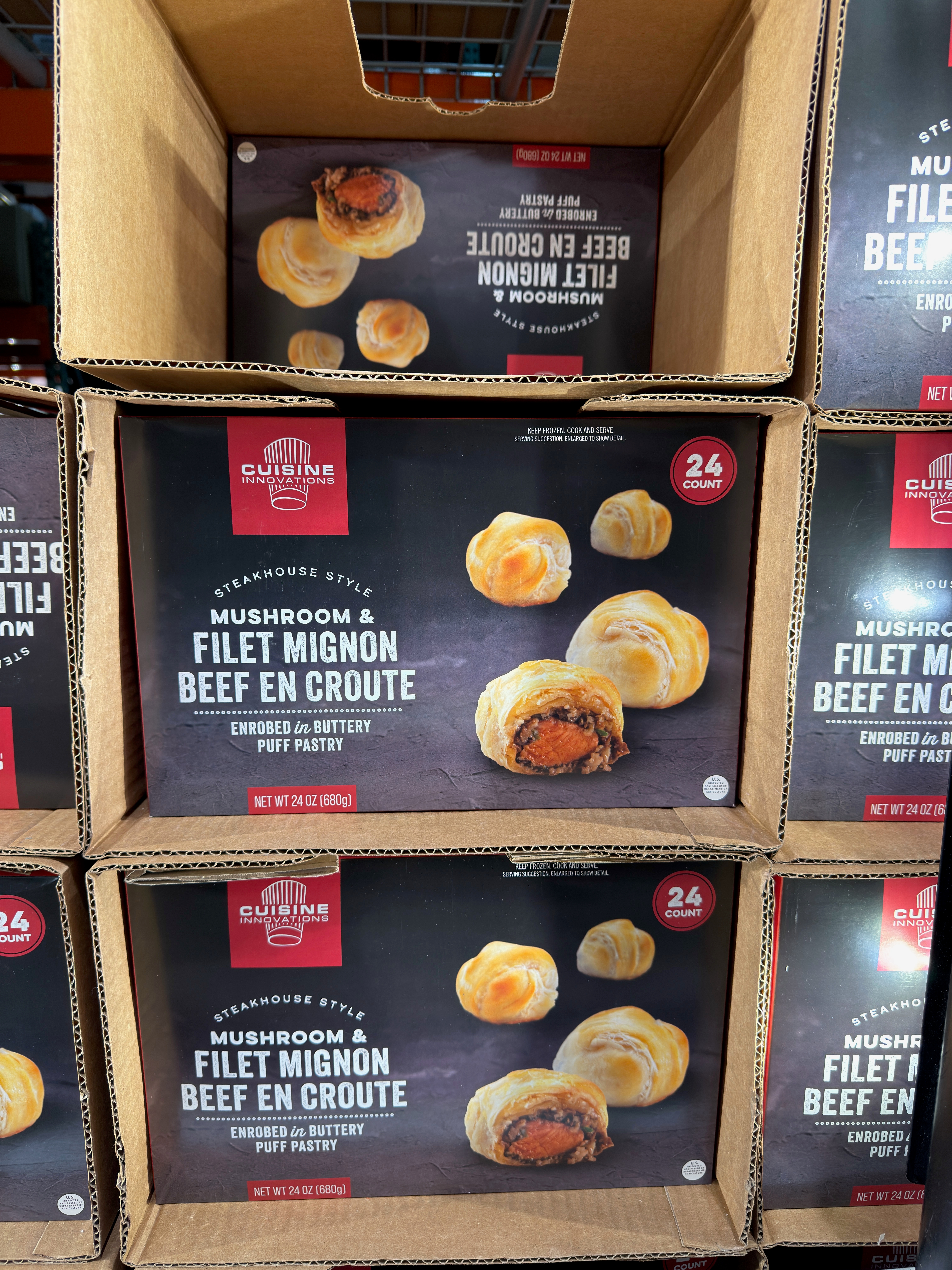 Boxes of beef en croute with visible packaging showing mushroom and filet mignon filling wrapped in puff pastry, stacked on a shelf