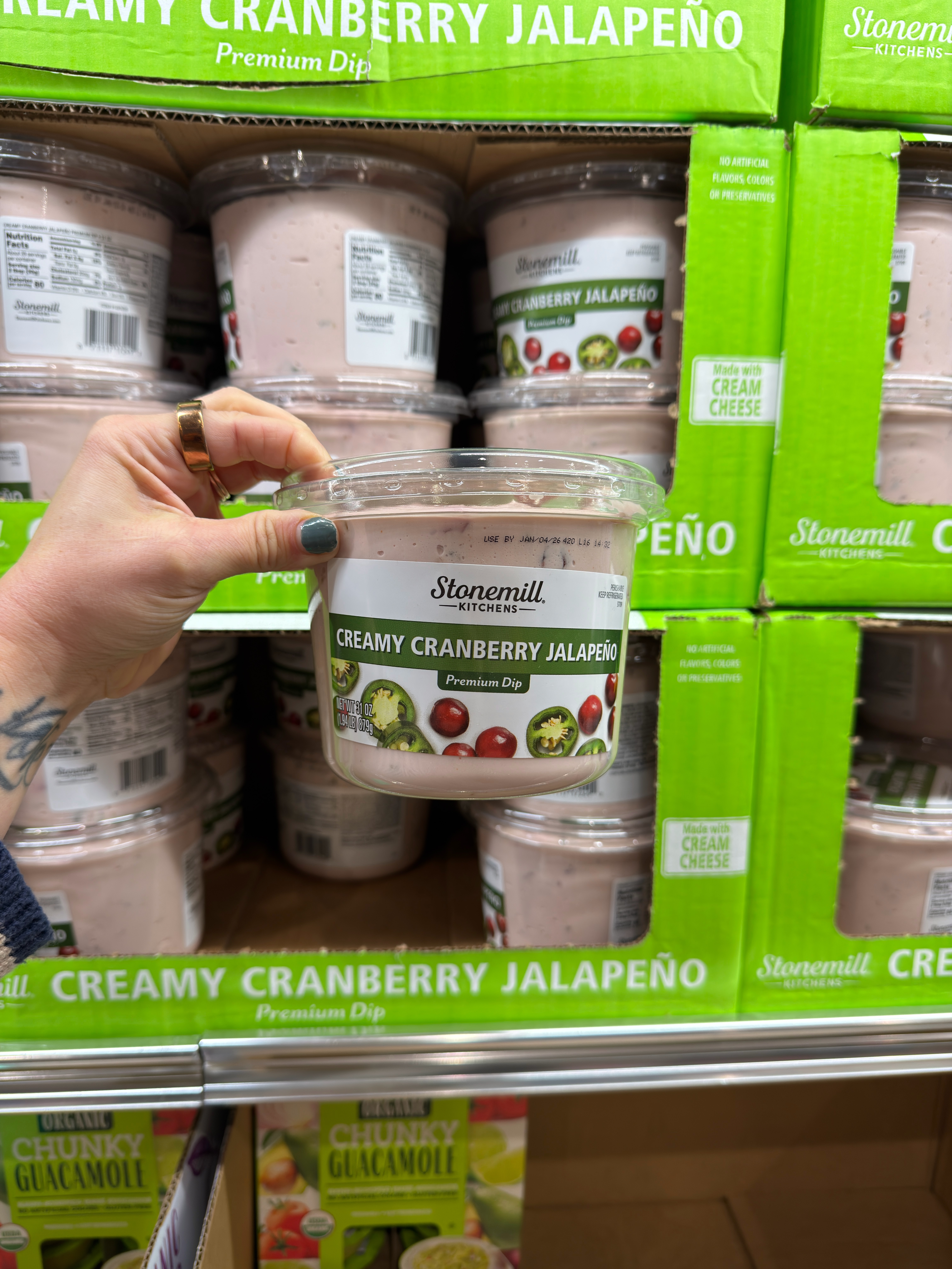A hand holds a container of Stonemill Kitchens' Creamy Cranberry Jalapeño Premium Dip in front of a store display with more of the same product