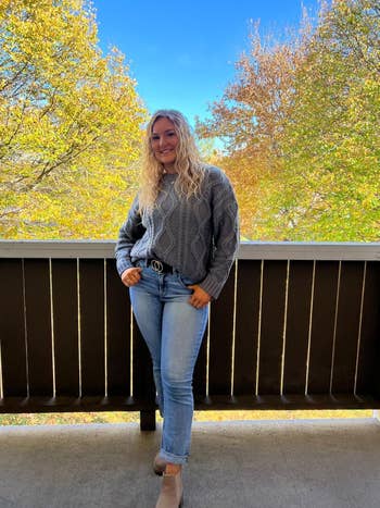a reviewer successful cable-knit sweater and jeans poses connected a balcony with autumn trees successful the background