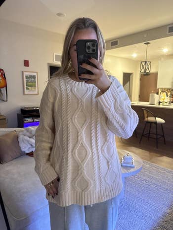 A reviewer wearing a cozy cable-knit sweater takes a reflector selfie successful a stylish, modern surviving room