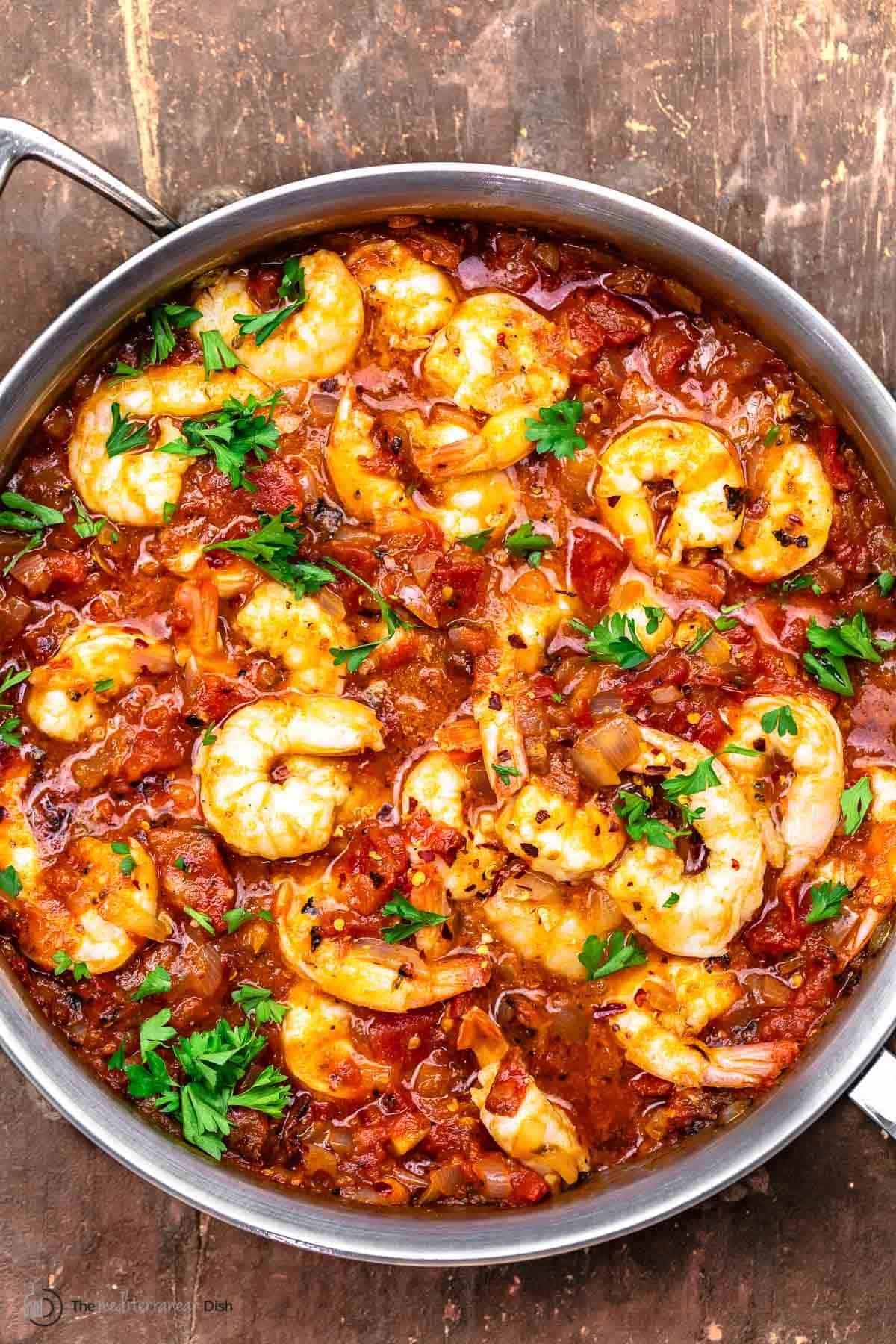 Shrimp stew with chopped tomatoes, onions, and herbs in a pot. Garnished with parsley