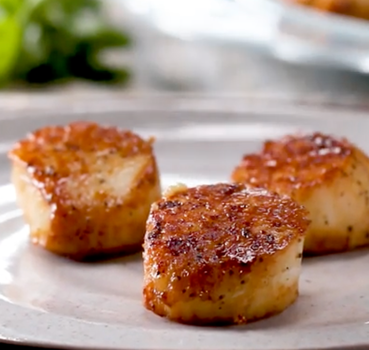 Three seared scallops are arranged on a plate, showcasing a caramelized exterior