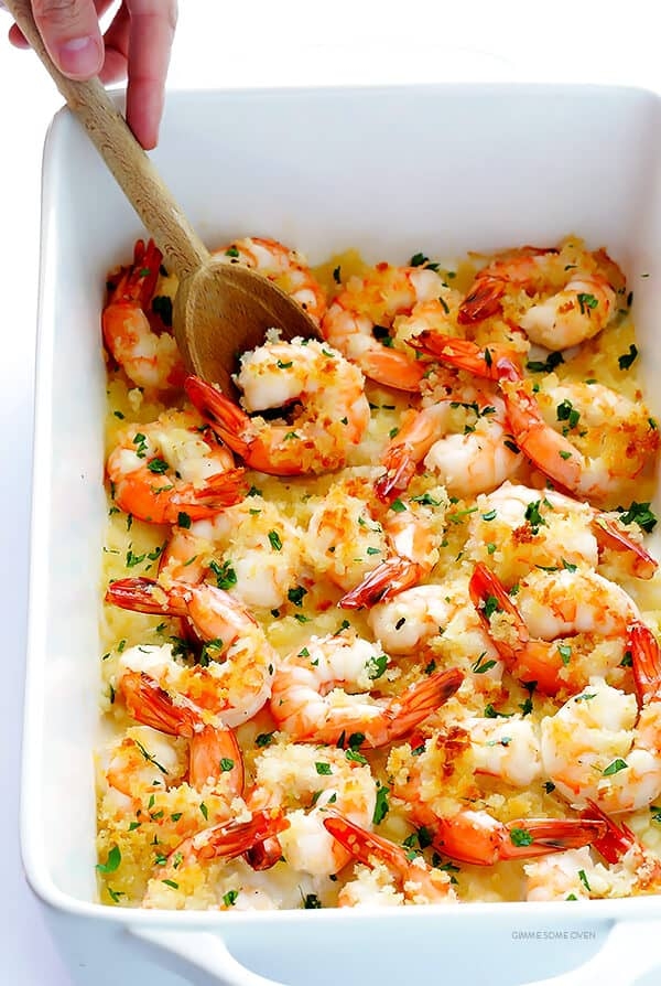 Baked shrimp casserole topped with breadcrumbs and herbs, with a wooden spoon serving a portion