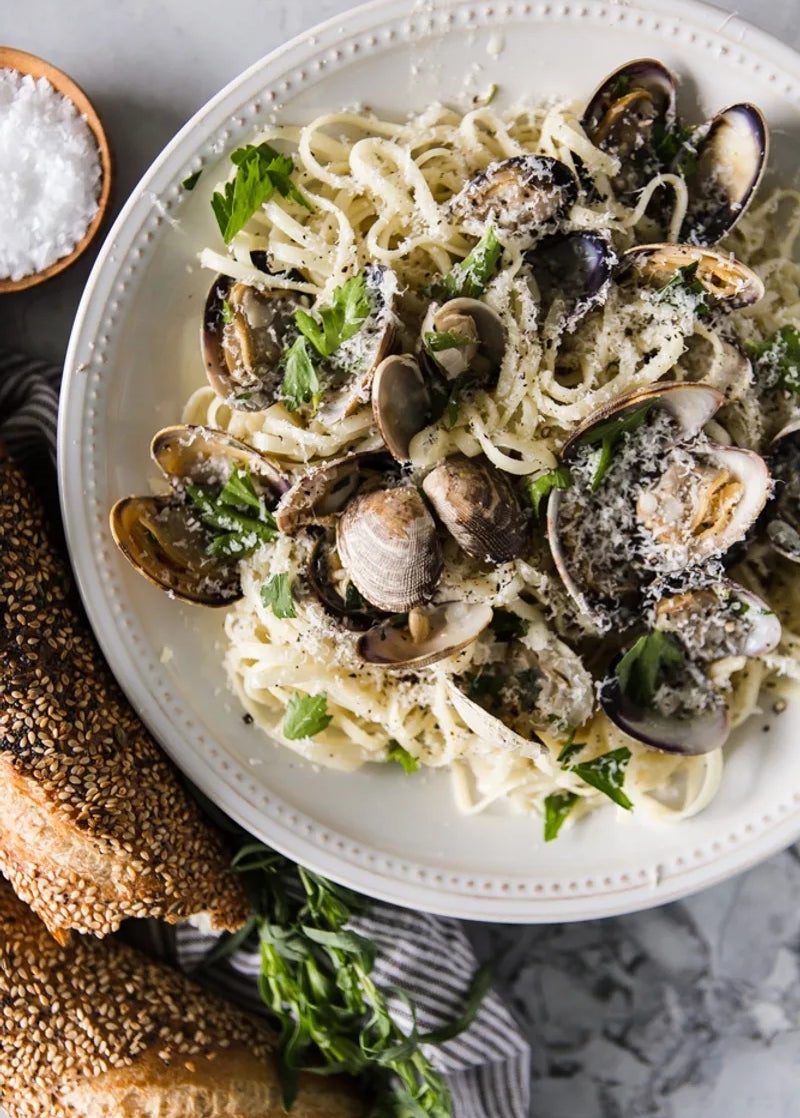 Pasta with clams in a creamy sauce, garnished with herbs and grated cheese. Served with two sesame-seed baguettes on the side