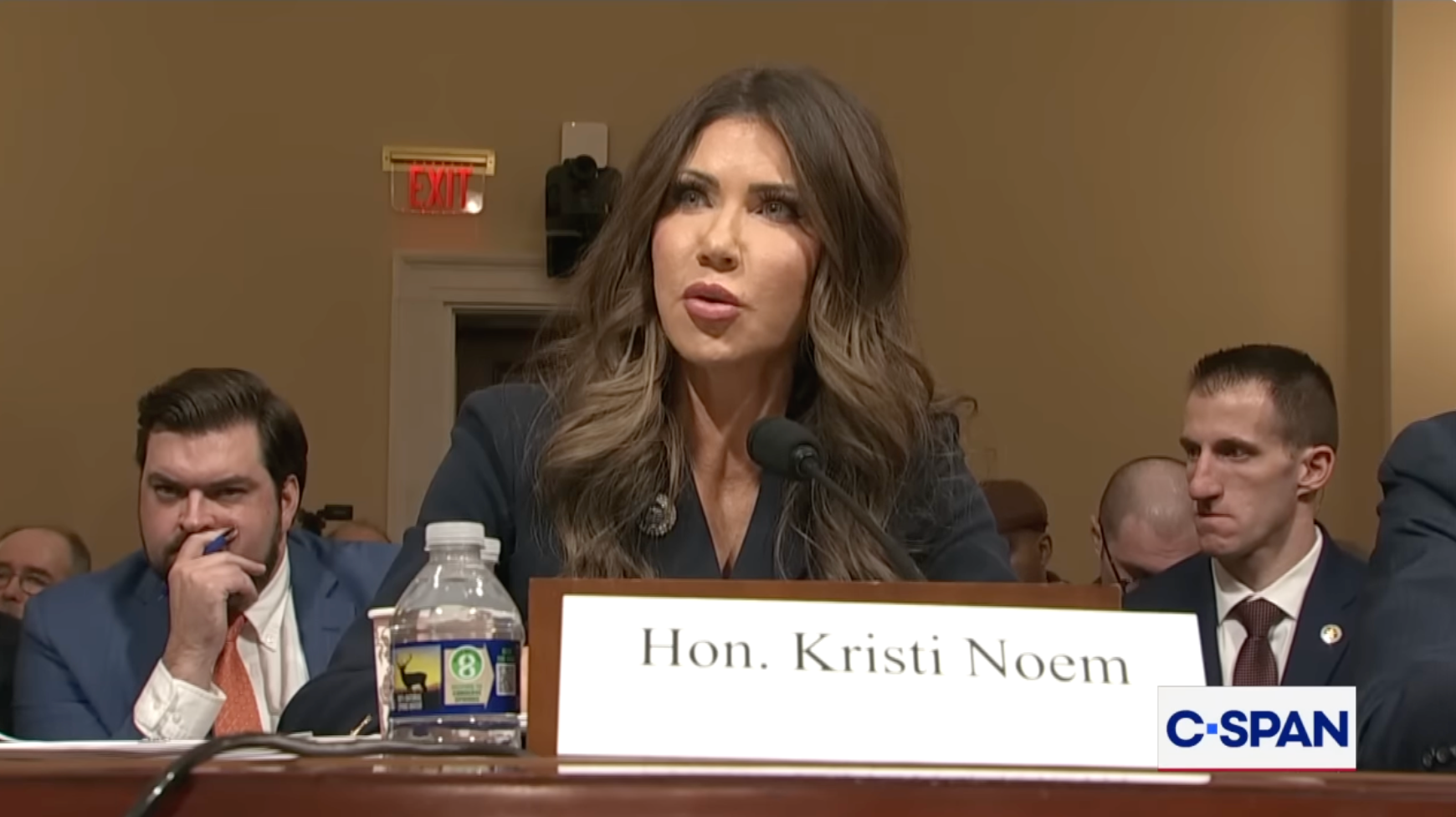 En kvinne taler under en regjeringshøring, sittende bak et navneskilt med teksten 