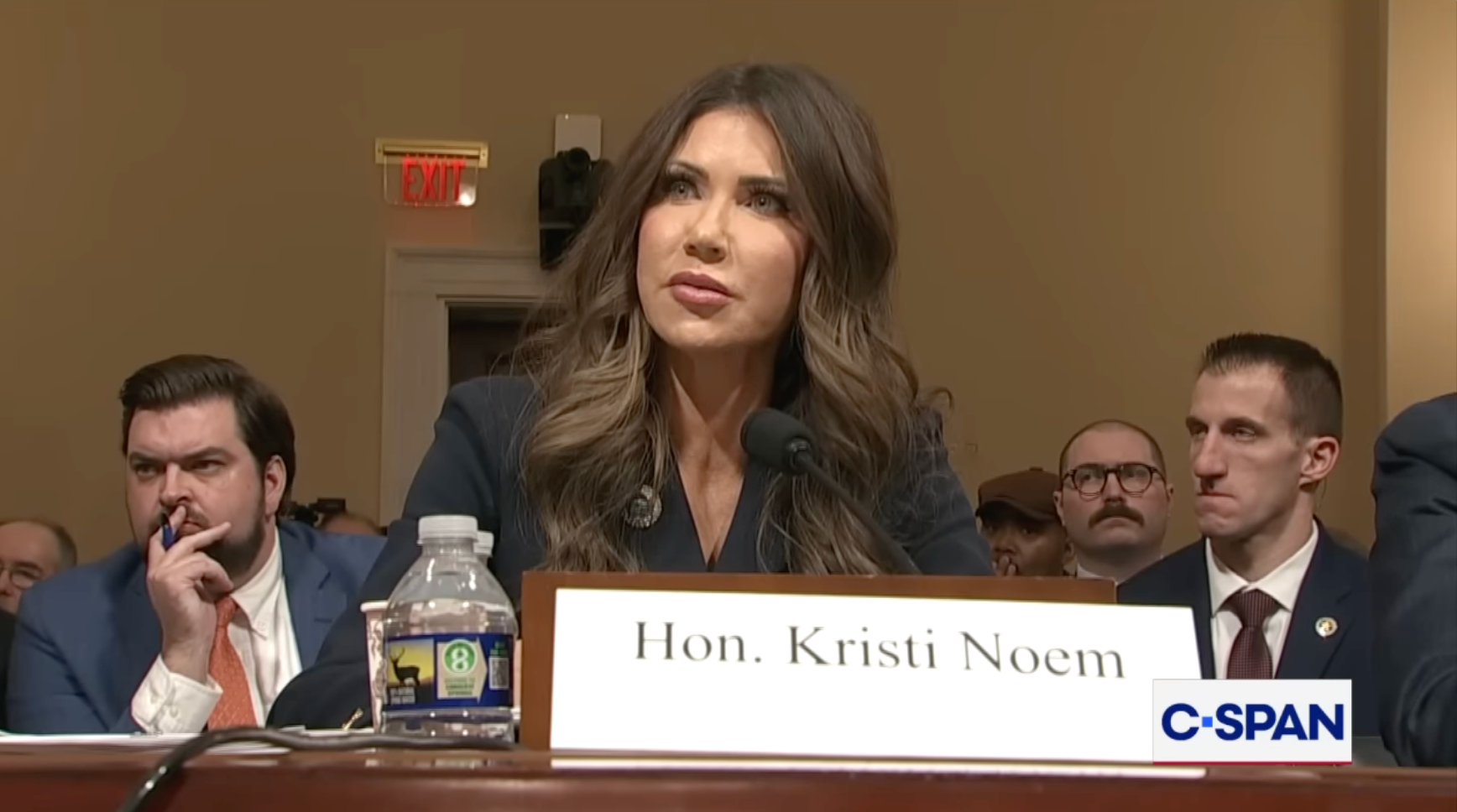 En kvinne, identifisert som Hon. Kristi Noem, vitner under en C-SPAN-dekket høring. Hun har på seg et formelt mørkt antrekk, sittende ved et bord med en mikrofon