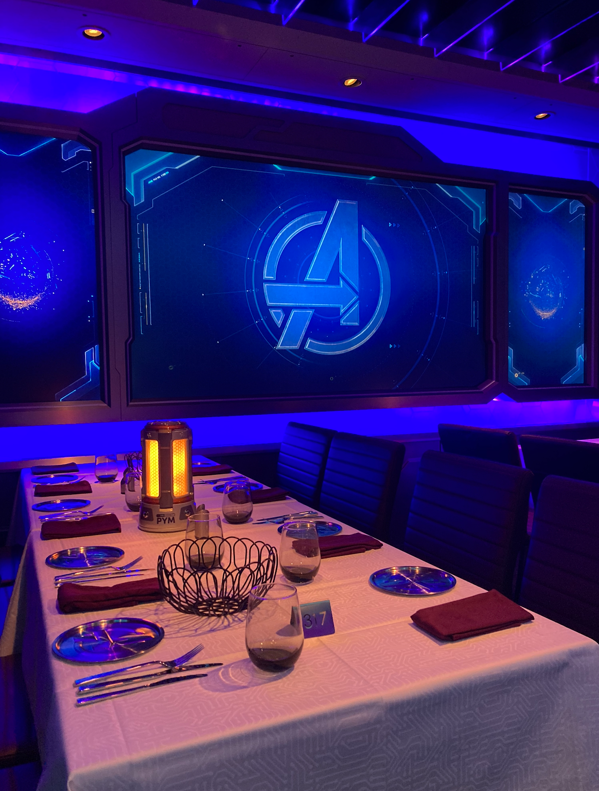Futuristic eating  setup with the Avengers logo connected  a ample  screen, featuring sleek tableware and a glowing centerpiece
