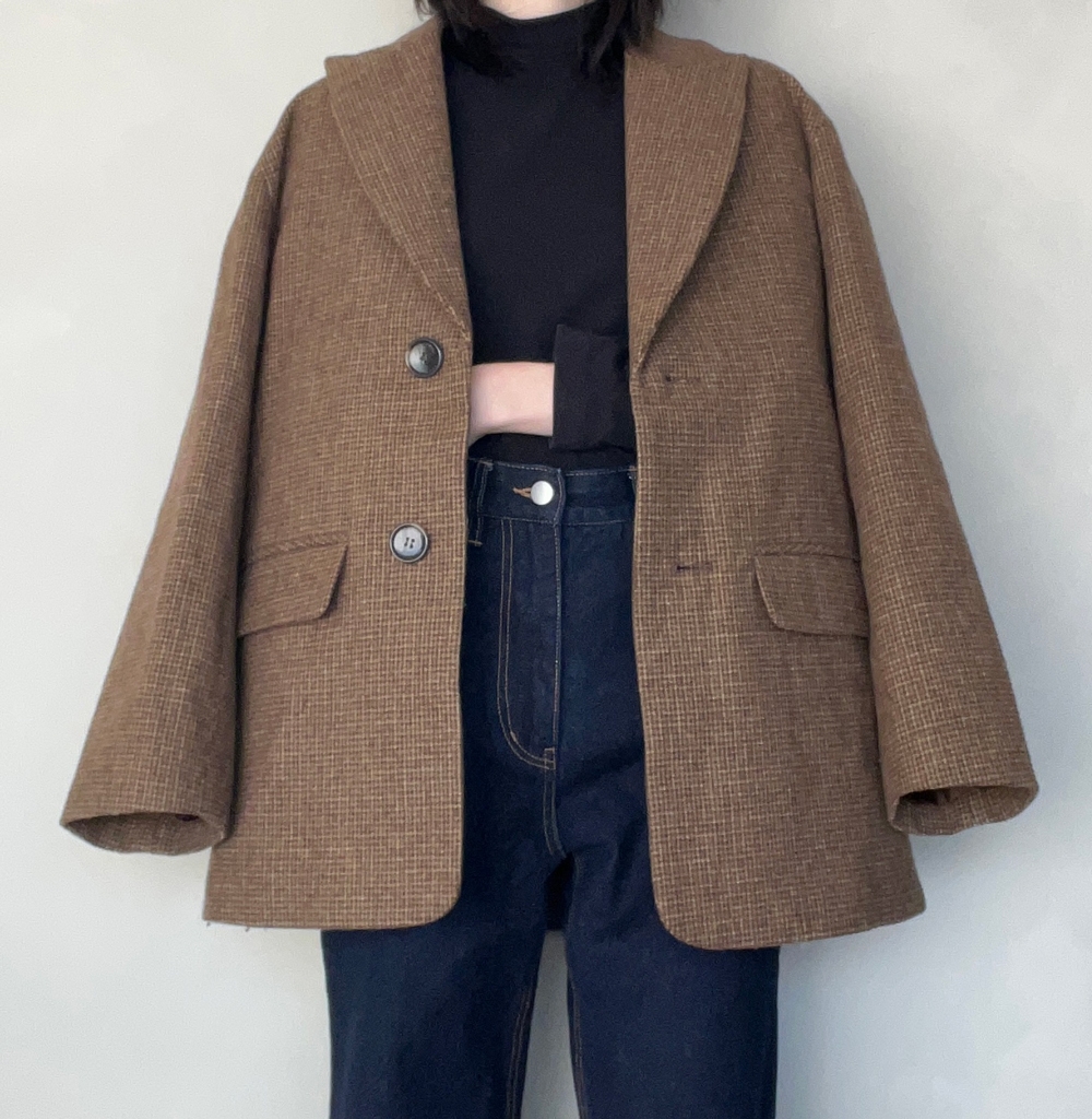 Person wearing an oversized blazer over a black top and high-waisted jeans, standing against a neutral background