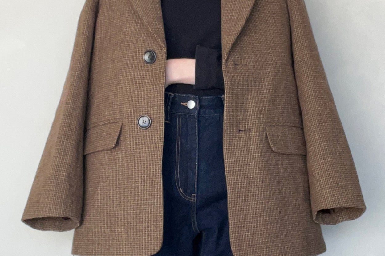 Person wearing an oversized blazer over a black top and high-waisted jeans, standing against a neutral background