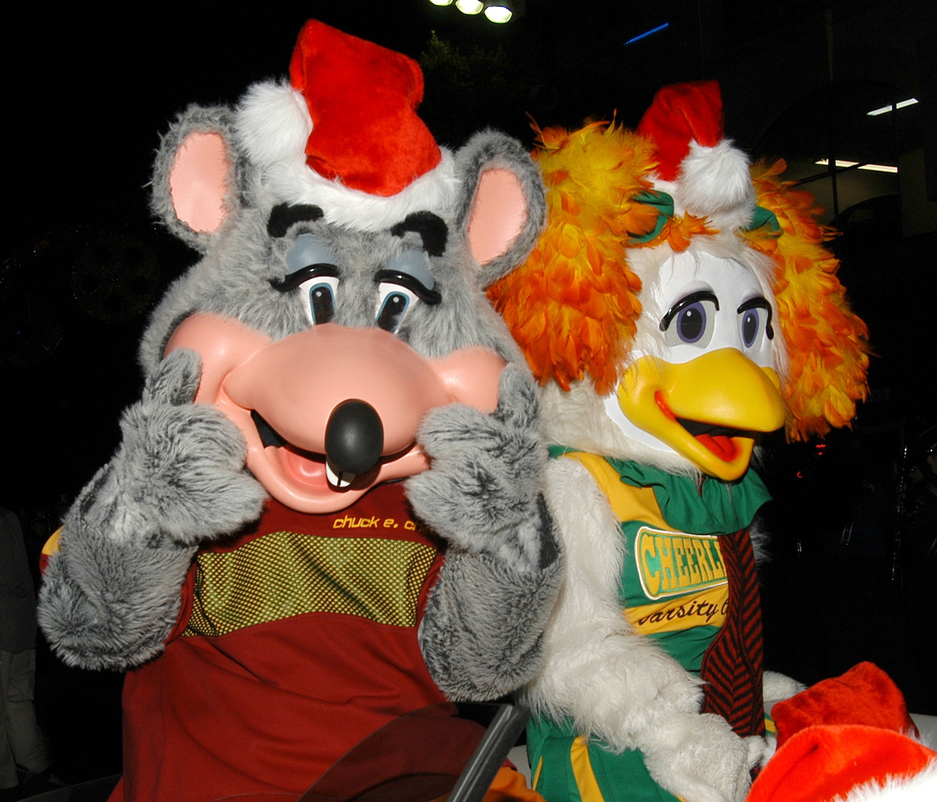 Two mascots dressed in festive attire, one mouse and one duck, pose with smiles at an event
