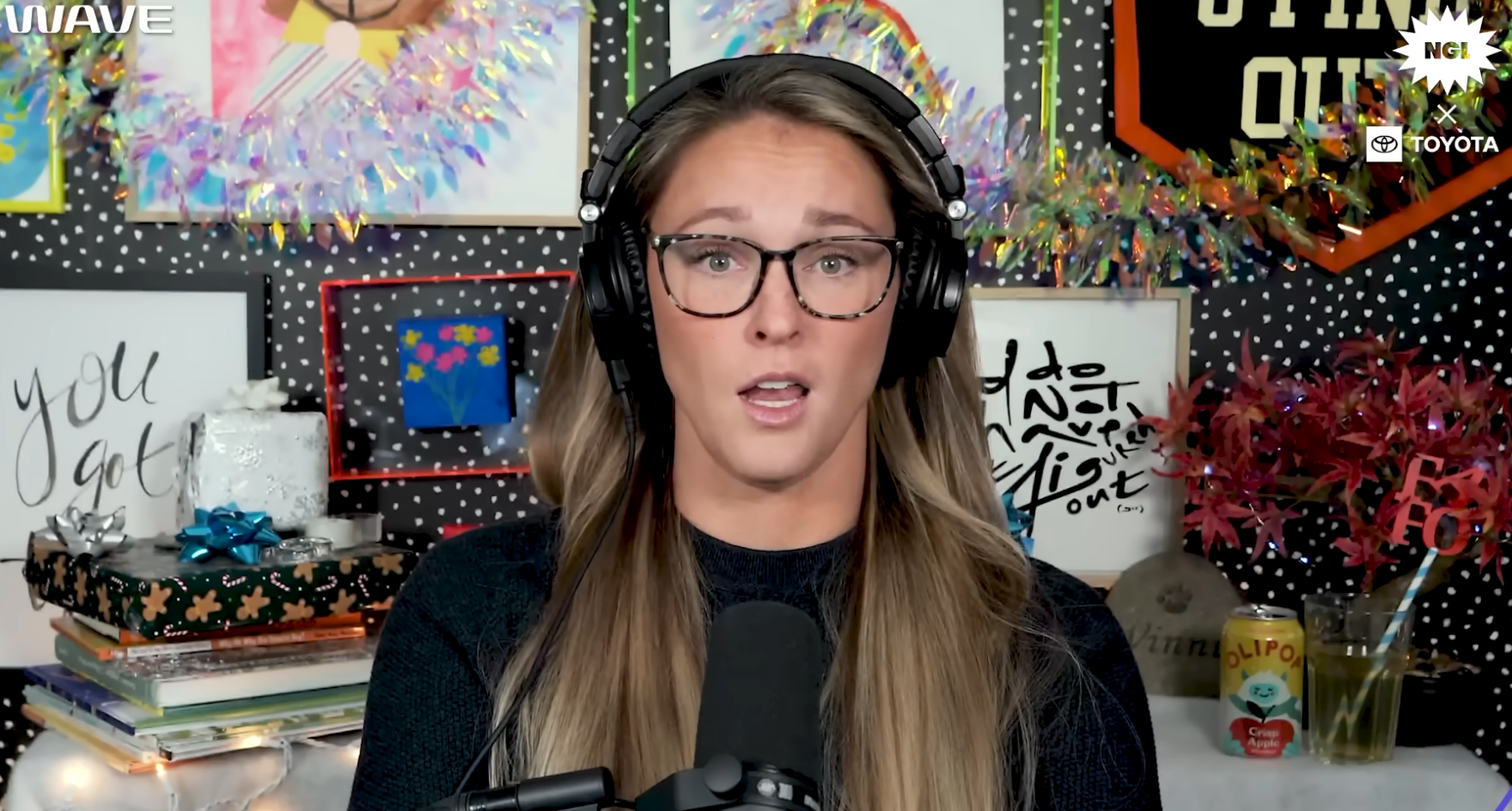 Person with glasses and headphones speaking successful  beforehand   of a microphone, surrounded by colorful decorations and books