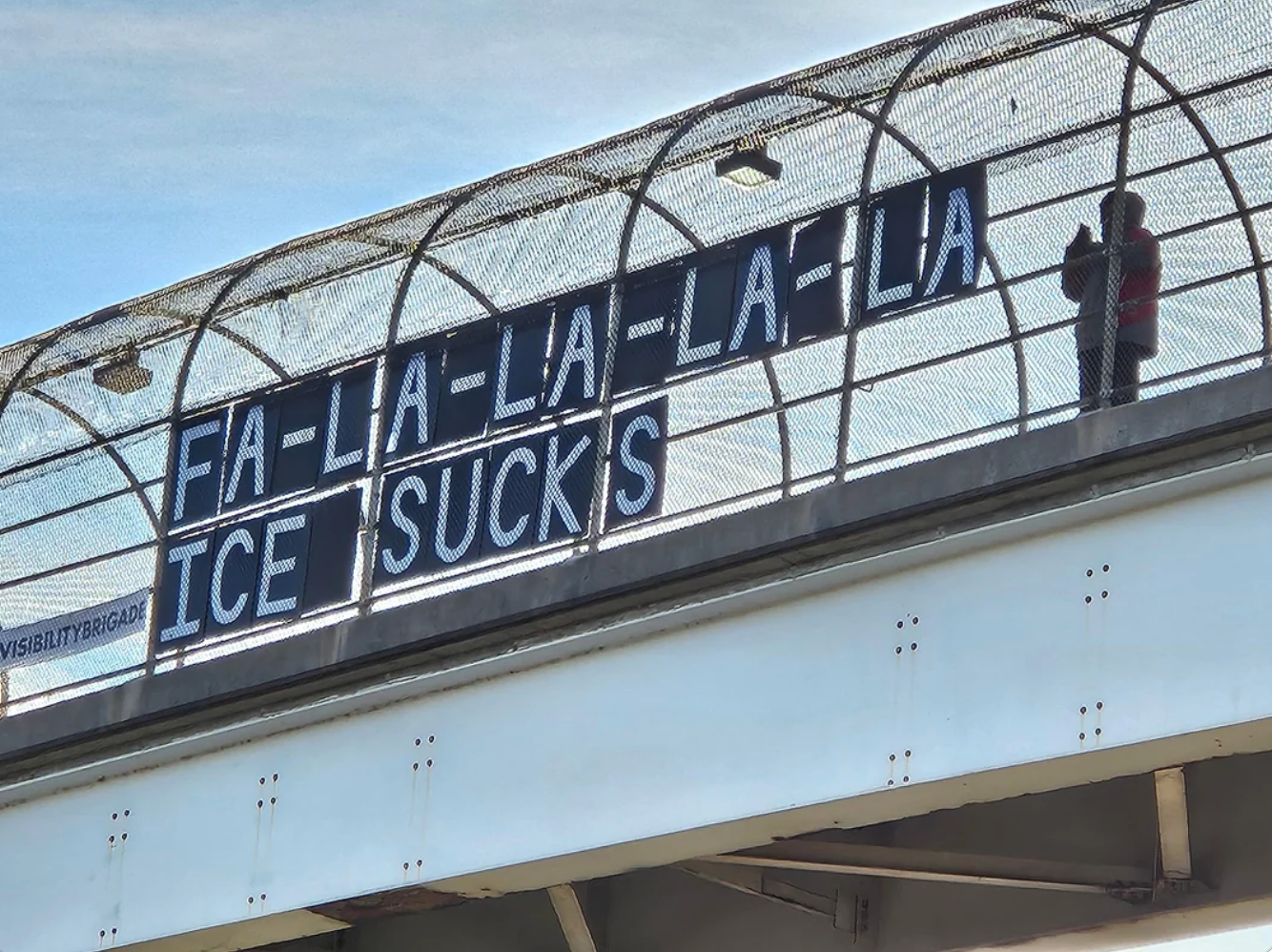 "FA-LA-LA-LA-LA ICE SUCKS," critiquing ICE. A idiosyncratic stands nearby