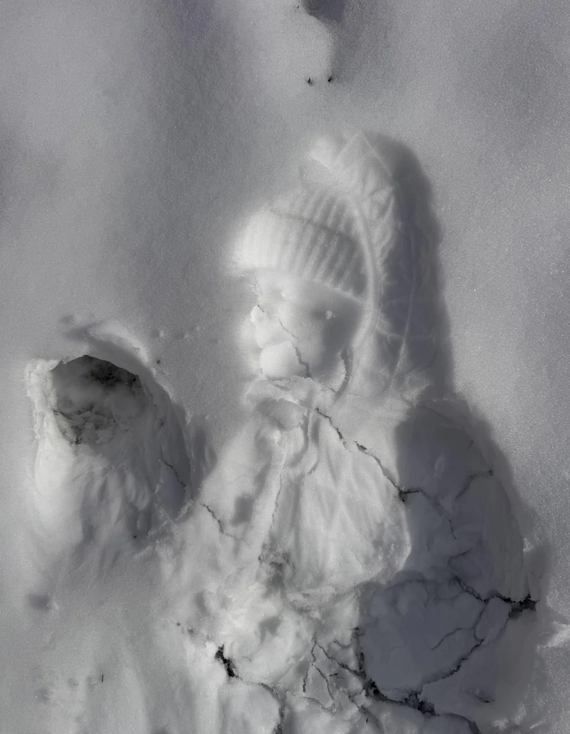 Snow imprint of a kid  wearing a knitted hat, coat, and scarf, lying connected  snowy ground, with disposable   tiny  handprint