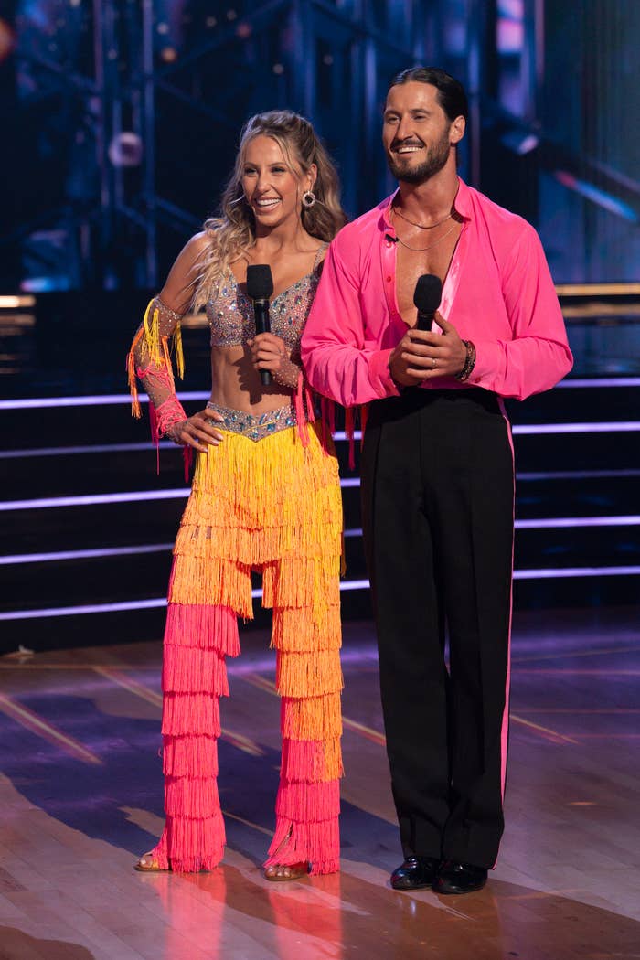 Two radical   connected  signifier    successful  creation   attire, some  holding microphones; the pistillate   wears a fringed outfit, the antheral   a matching unfastened  garment  and pants