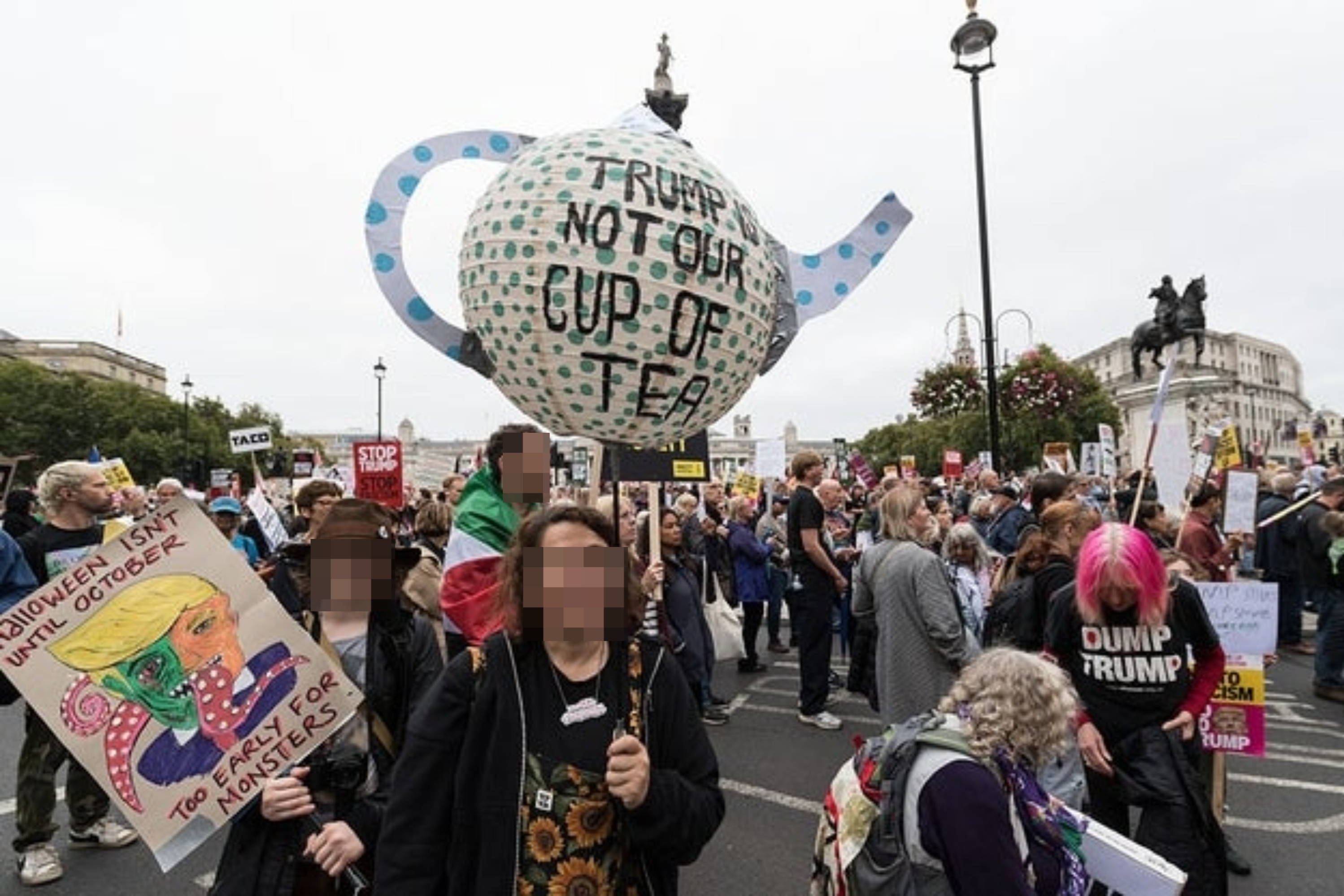 Folk ved en protest holder skilt, inkludert en stor tekanneformet med teksten «Trump Not Our Cup of Tea»; under en demonstrasjon