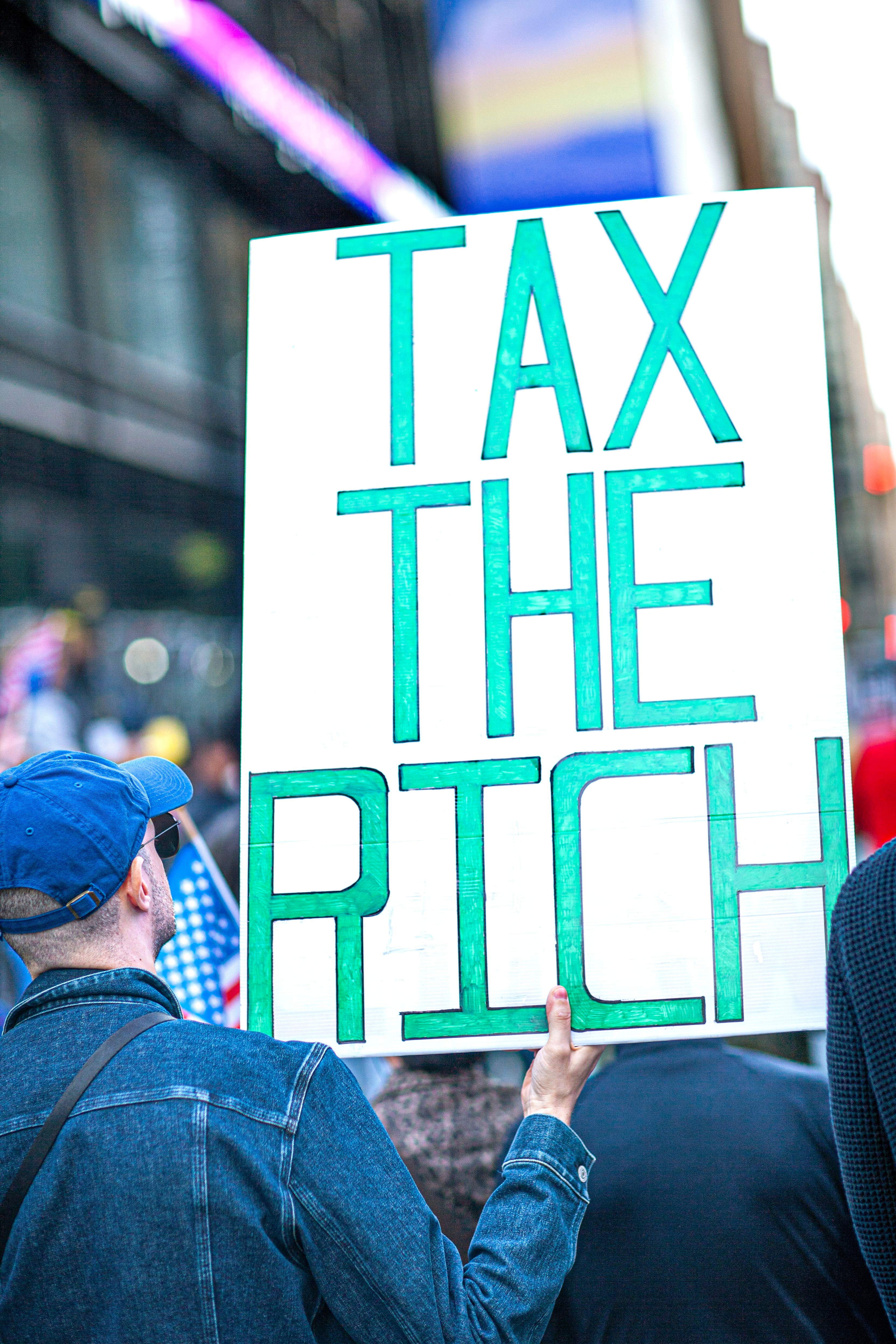 Demonstranten holder et stort skilt med teksten «TAX THE RICH»; på en offentlig demonstrasjon