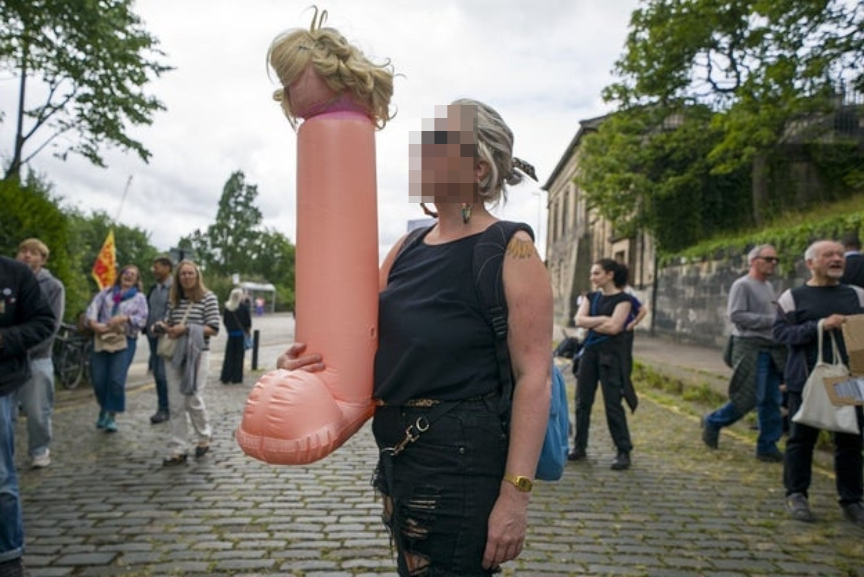 En kvinne holder en oppblåsbar gjenstand på et offentlig arrangement, omgitt av tilskuere på en brosteinsgate