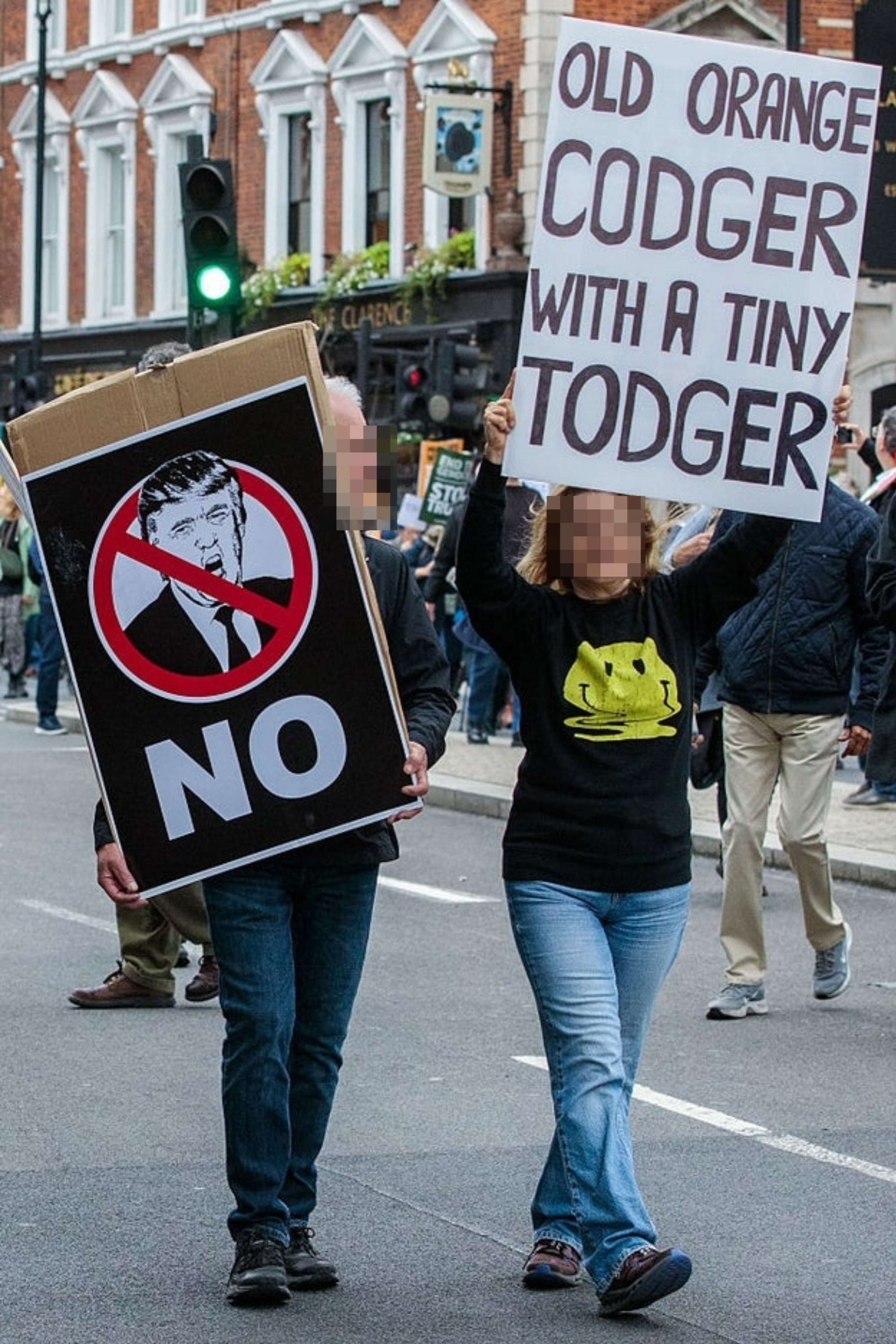 Demonstranter bærer skilt, ett med et overkrysset bilde av en offentlig person og «NEI»; den andre leser 