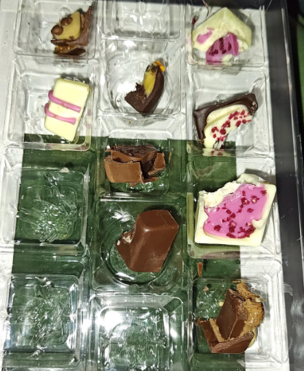 Empty cocoa container with breached pieces and a fewer remaining chocolates with assorted toppings and fillings