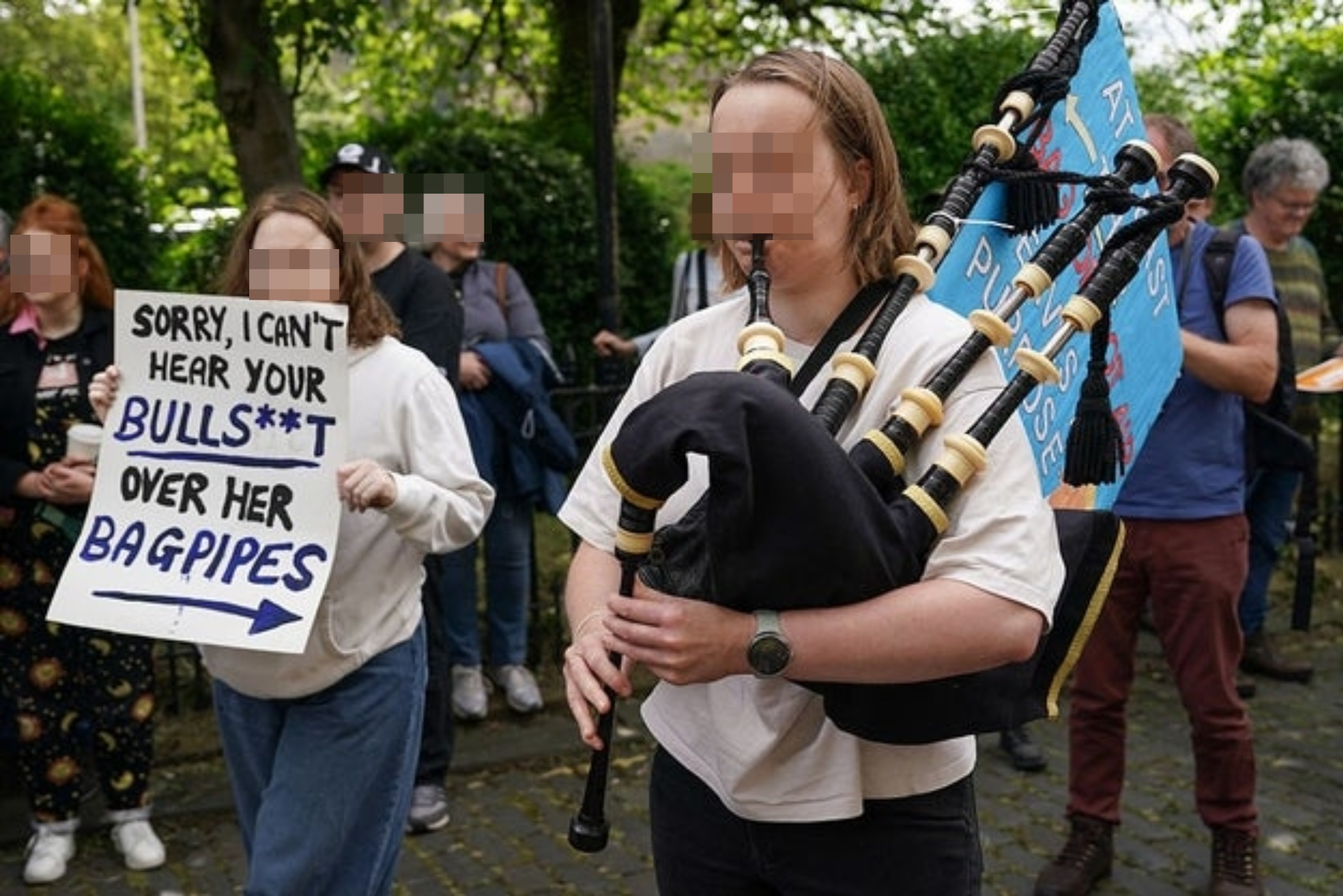 Person som spiller sekkepipe ved en protest; en annen holder et skilt med teksten 