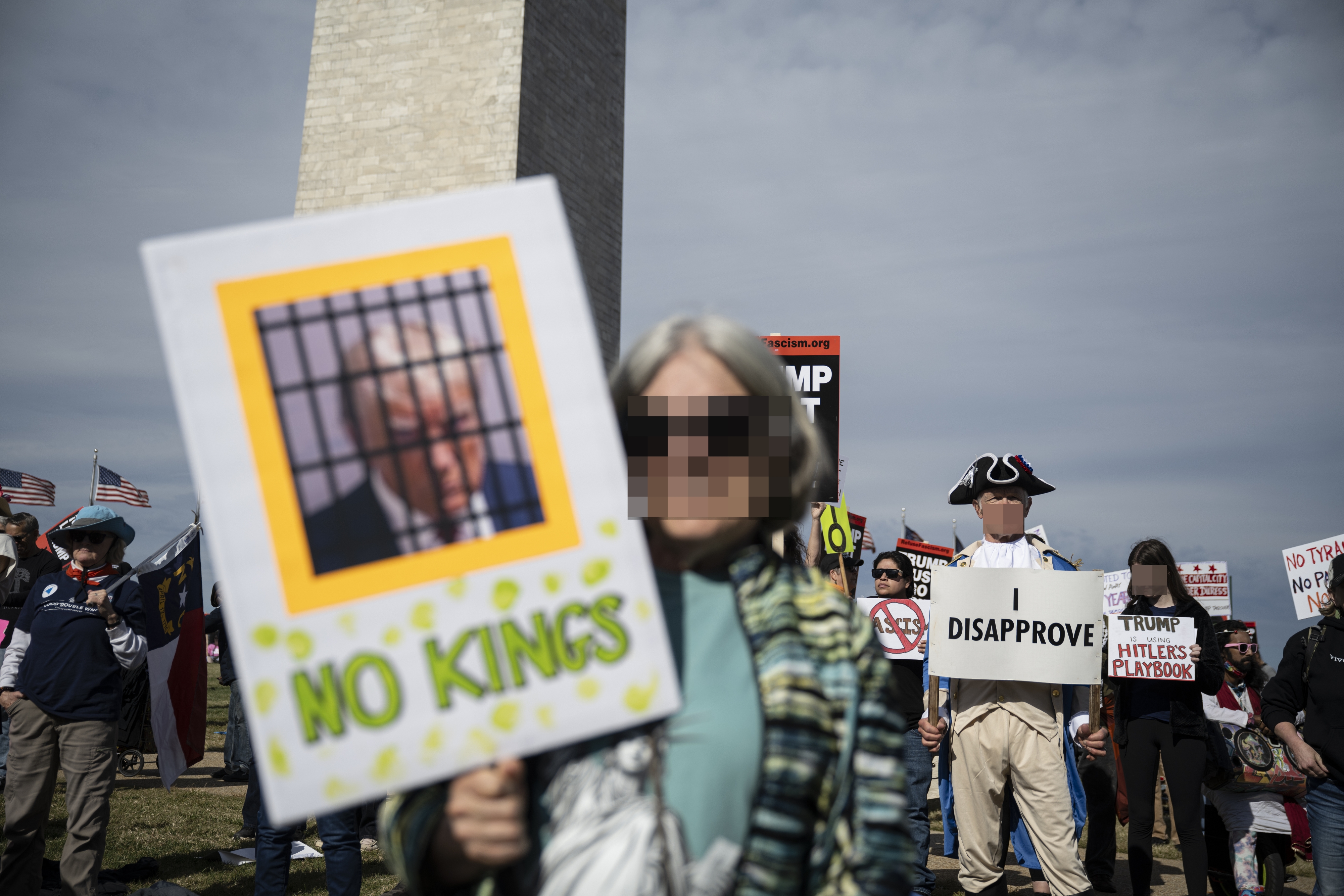 Folk protesterer i nærheten av et monument og holder skilt som 