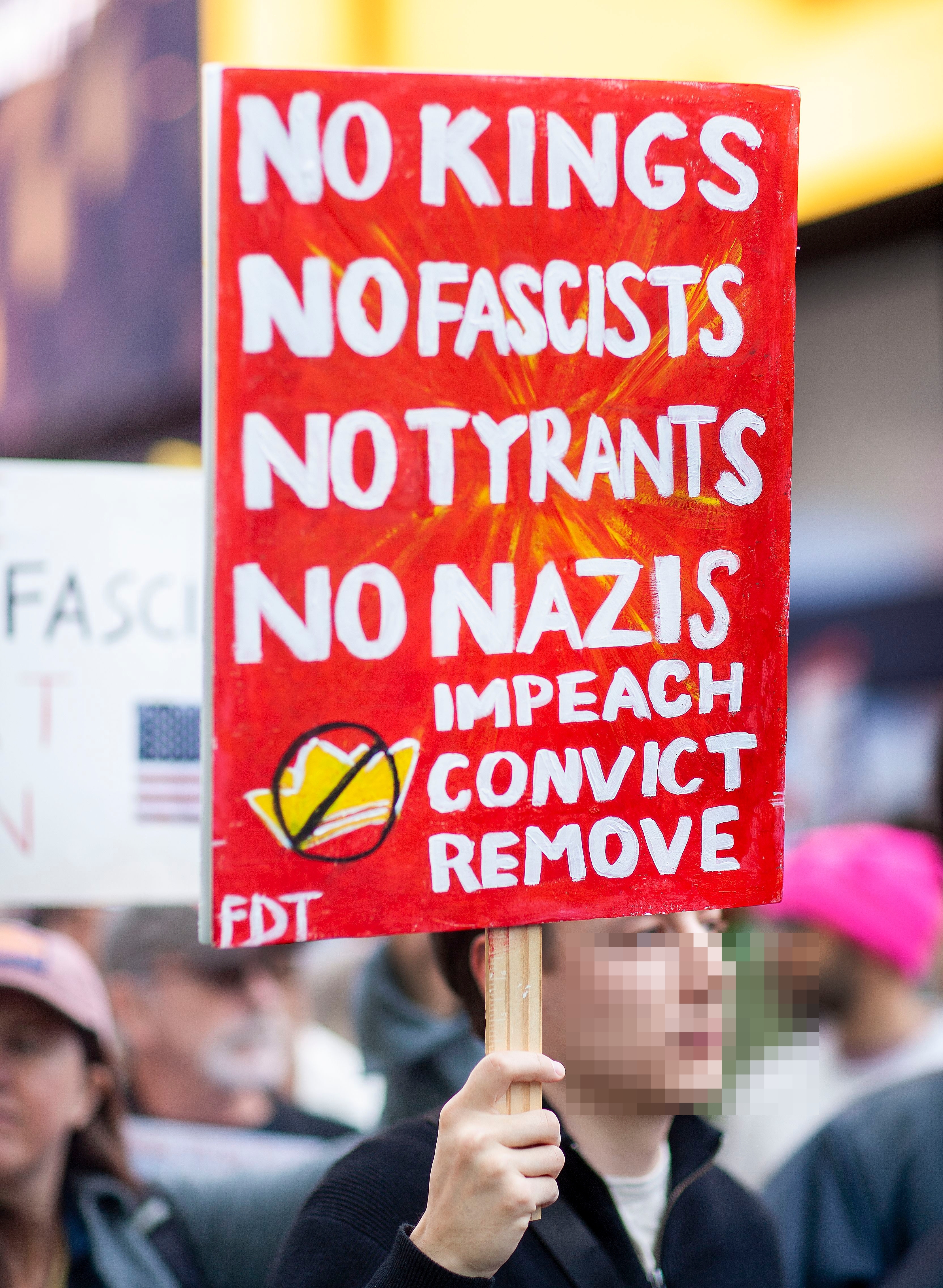 Demonstranten holder et skilt der det står «Ingen konger, ingen fascister, ingen tyranner, ingen nazister. Anklage, dømme, fjerne" på et rally, med folk i bakgrunnen