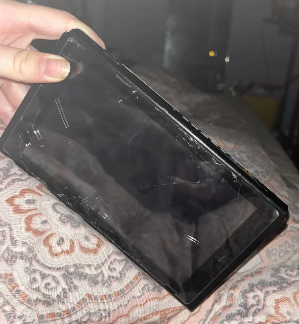 A person's manus holds a visibly cracked portable gaming console surface implicit a patterned cloth backdrop