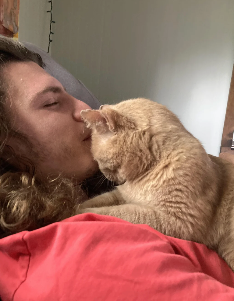 Person relaxing connected  a couch, smiling with eyes closed, portion    a feline  sits connected  their chest, looking astatine  them affectionately