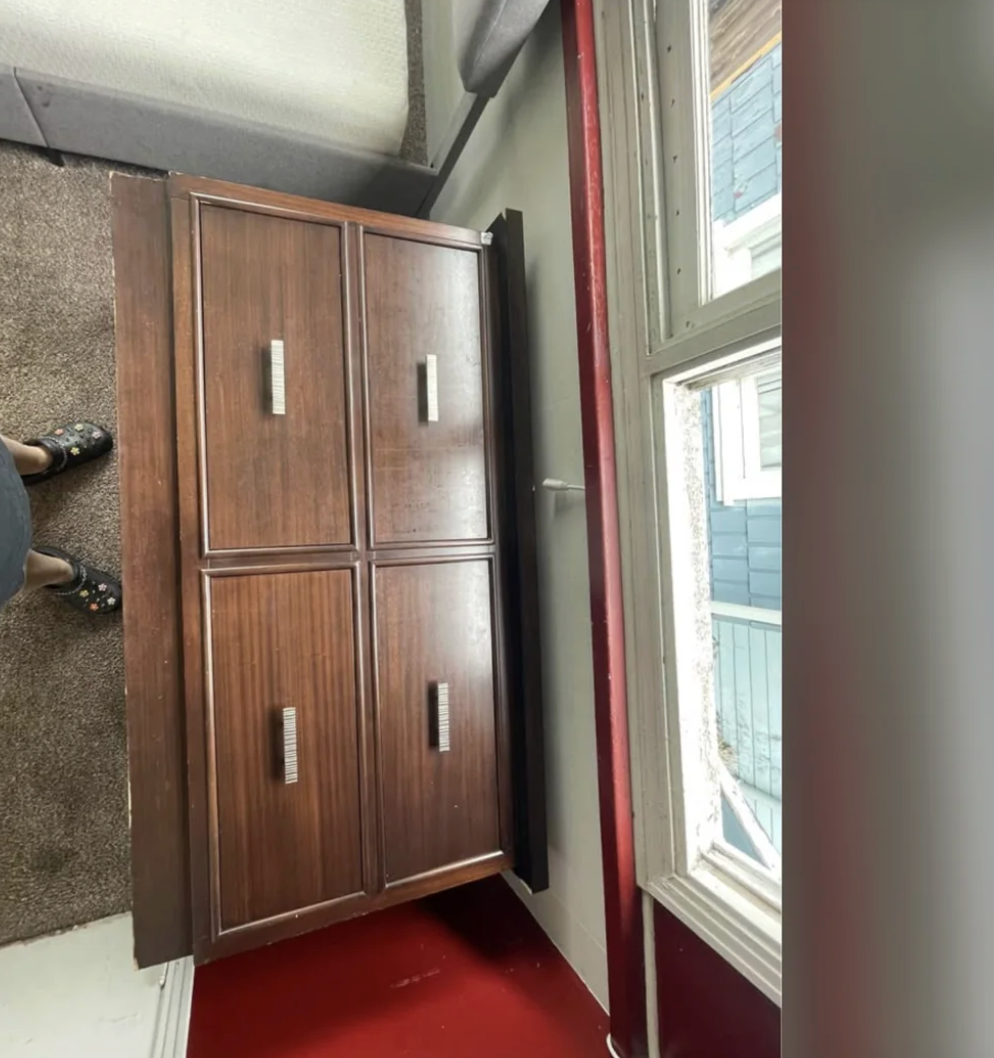 Wooden furniture  with 4  paneled doors adjacent  to a window. Person's feet successful  sandals disposable   adjacent   bottommost  left