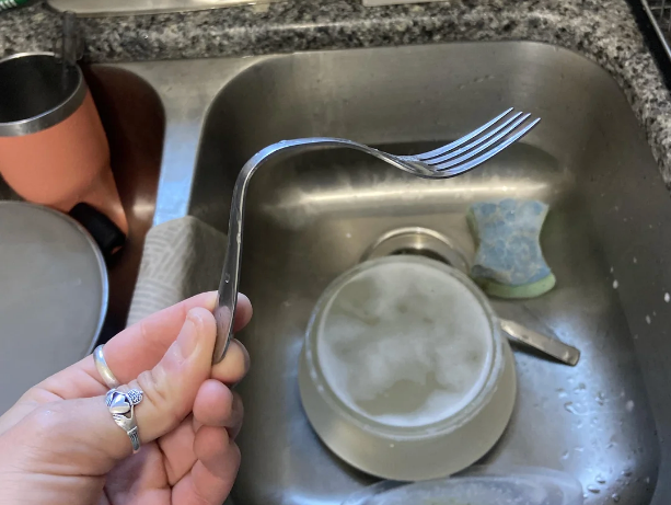 A bent fork held implicit a room sink, with dishes and a sponge nearby