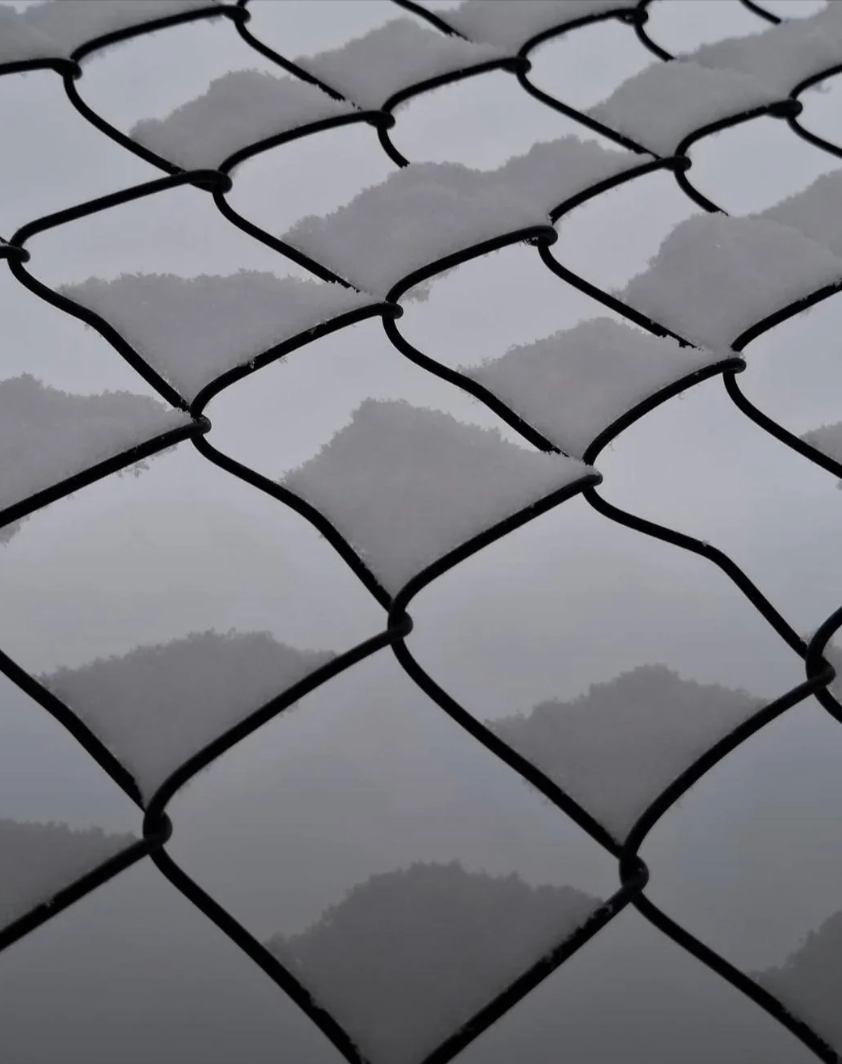 Close-up of a chain-link obstruction   with snowfall  connected  the wires, creating a patterned texture