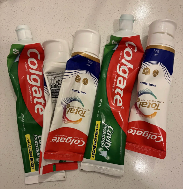 Five half-full toothpaste tubes, including Colgate and Total, are randomly placed connected a surface