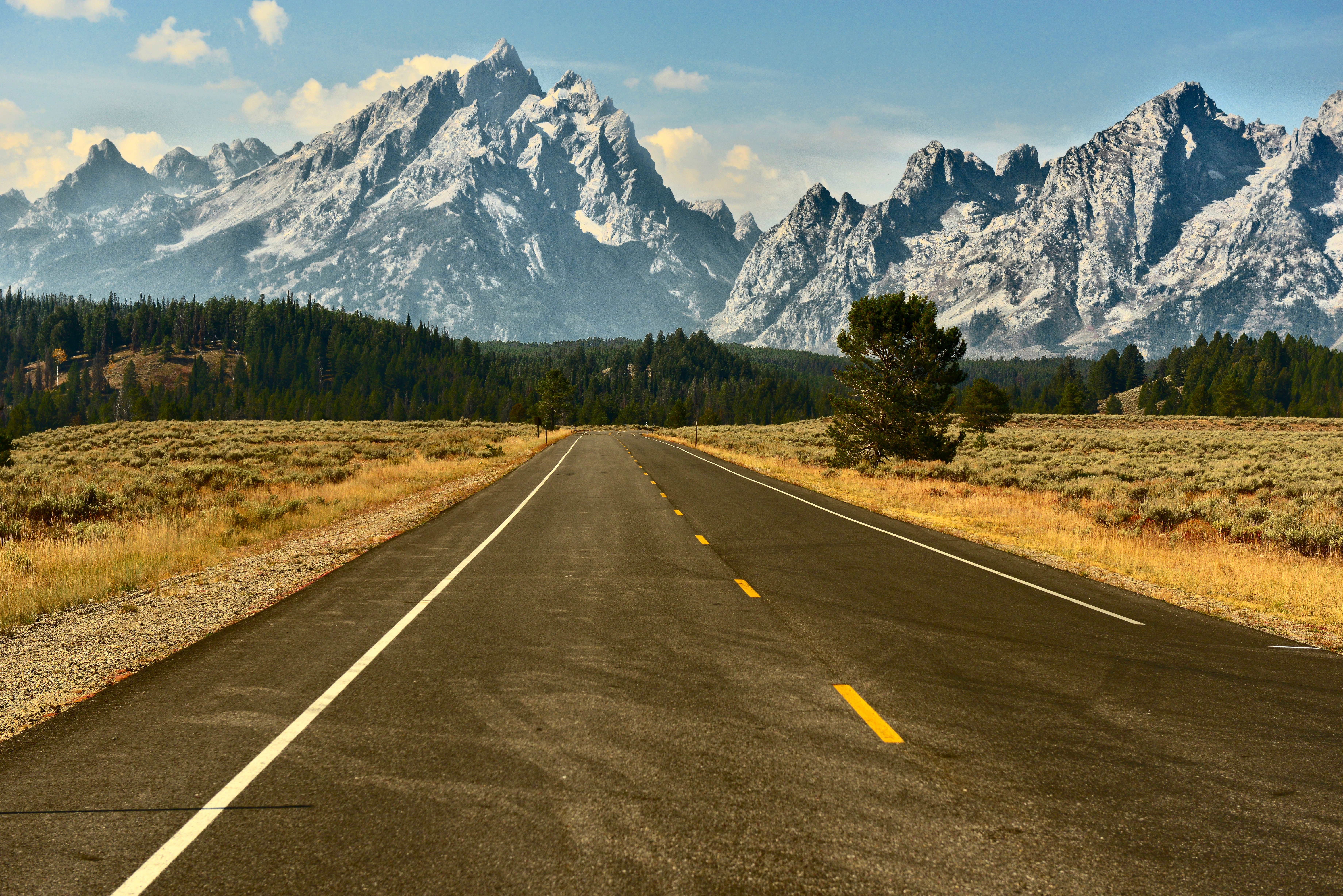 Vakker utsikt over en tom vei som fører mot snødekte fjell under klar himmel