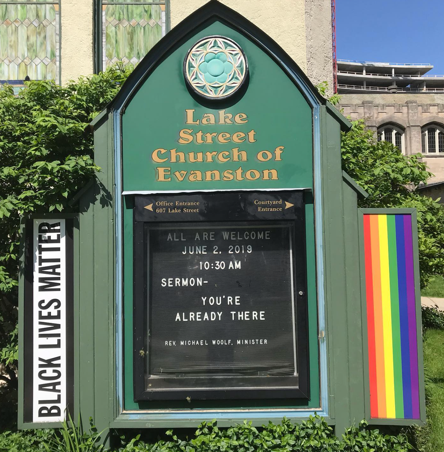 Kirkeskiltet lyder: «Alle er velkommen. 2. juni 2019, 10:30. Preken – du er allerede der. Rev. Michael Wolf, minister." Black Lives Matter-banner i nærheten