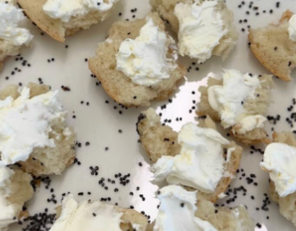 Bagel pieces topped with cream cheese, scattered with poppy seeds on a plate