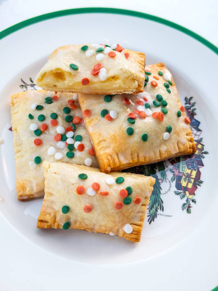 Pastries on a decorative plate, topped with festive sprinkles; one is cut open, revealing a fruity filling