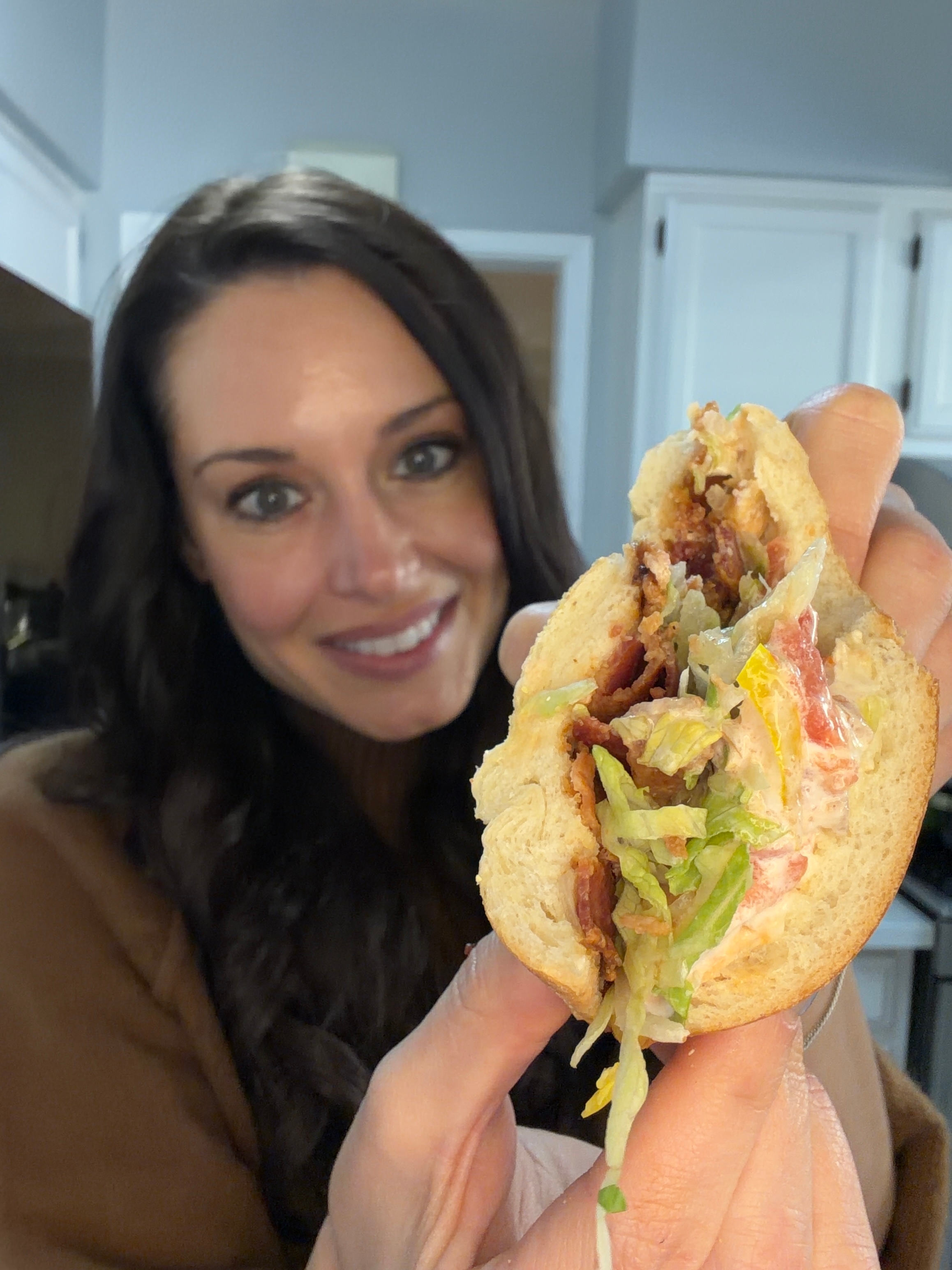 Woman smiling and holding a sandwich with visible lettuce and fillings