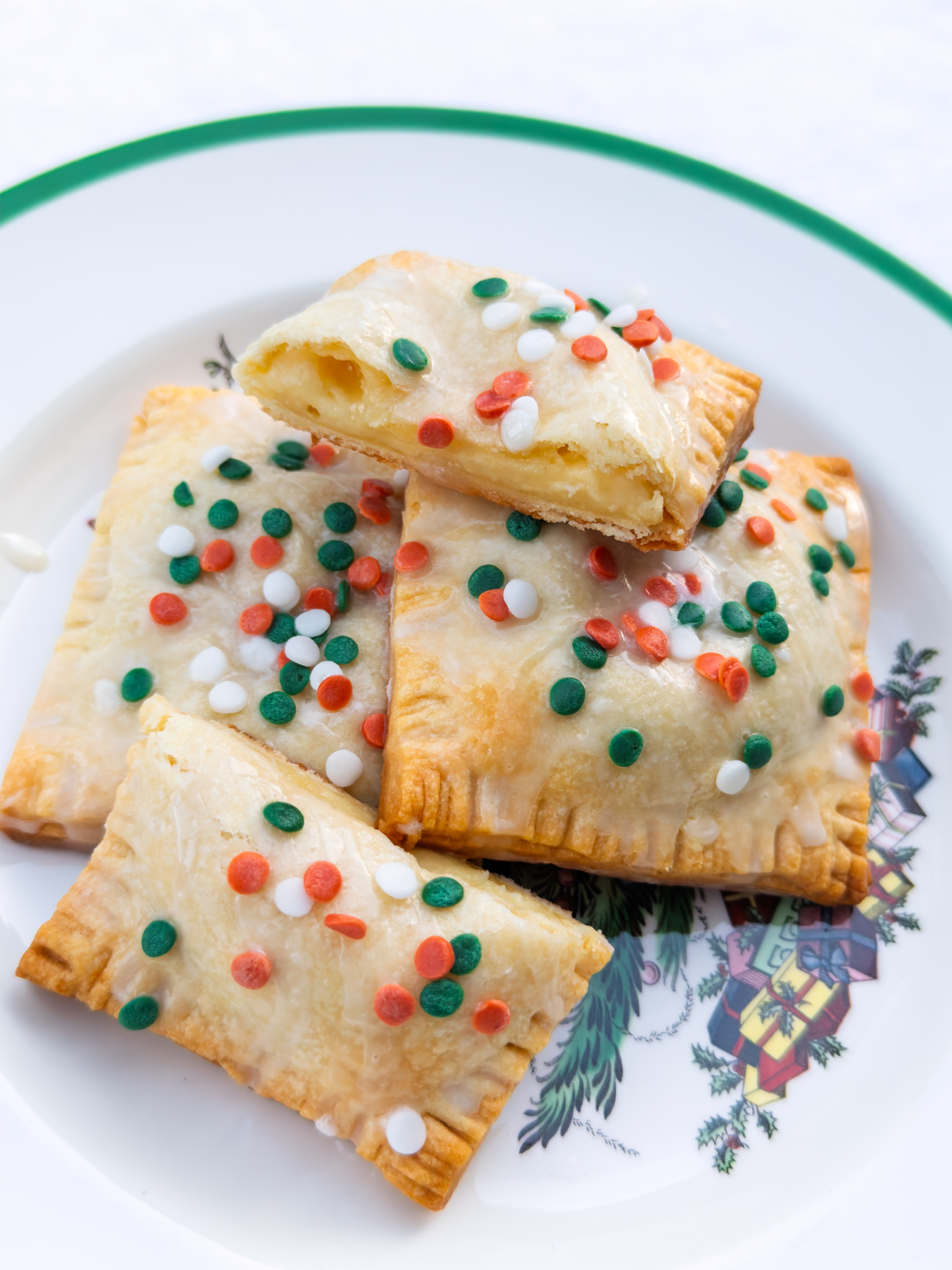 Four frosted pastries with red, green, and white sprinkles on a decorative plate. One pastry is partially eaten, revealing a filling