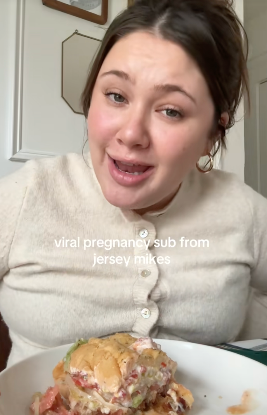 Person smiling while seated at a table with a partially eaten sandwich labeled "viral pregnancy sub from Jersey Mike's."